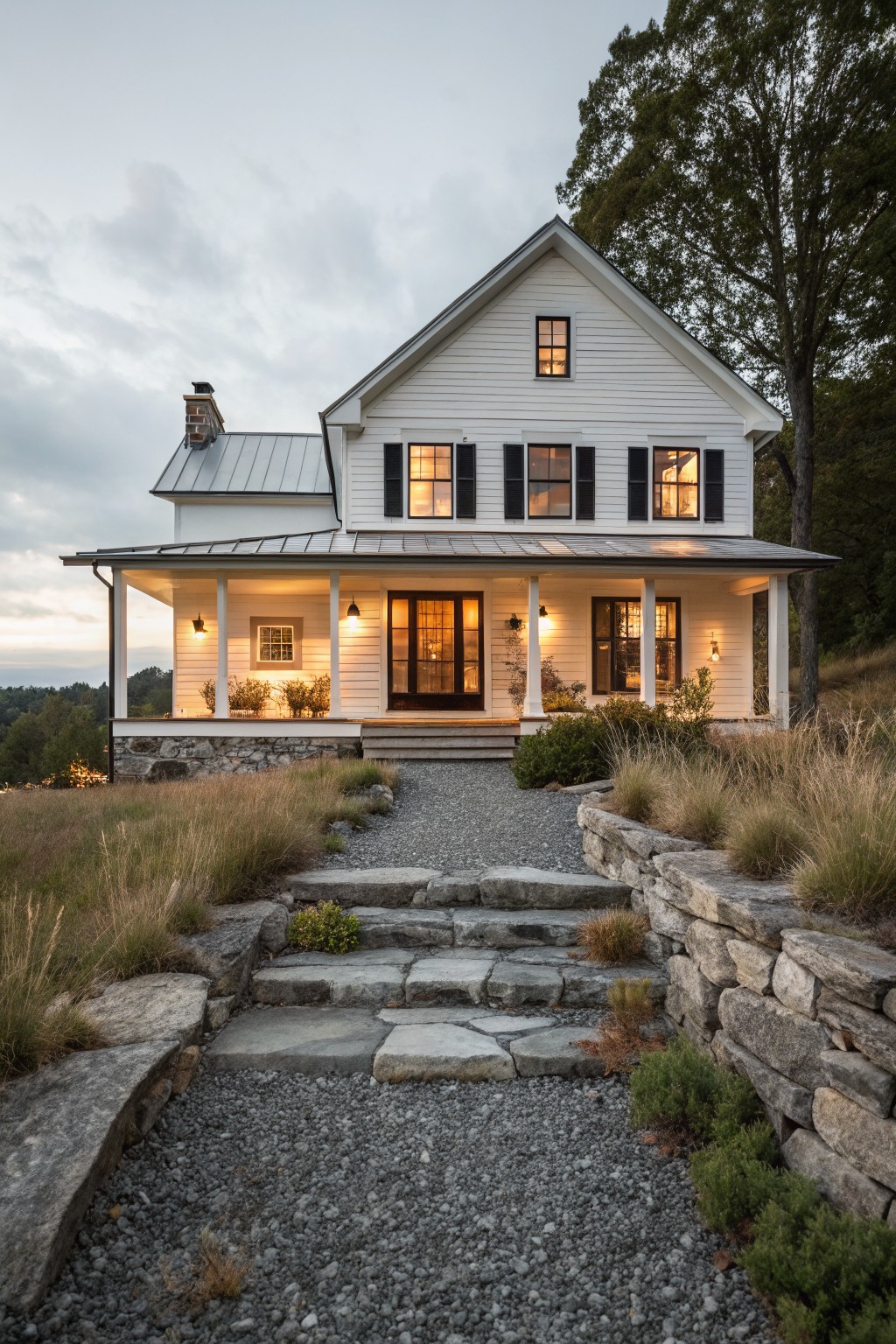 A white two-story farmhouse with a stone foundation, front porch, gravel path, and stone steps leading to the entrance.