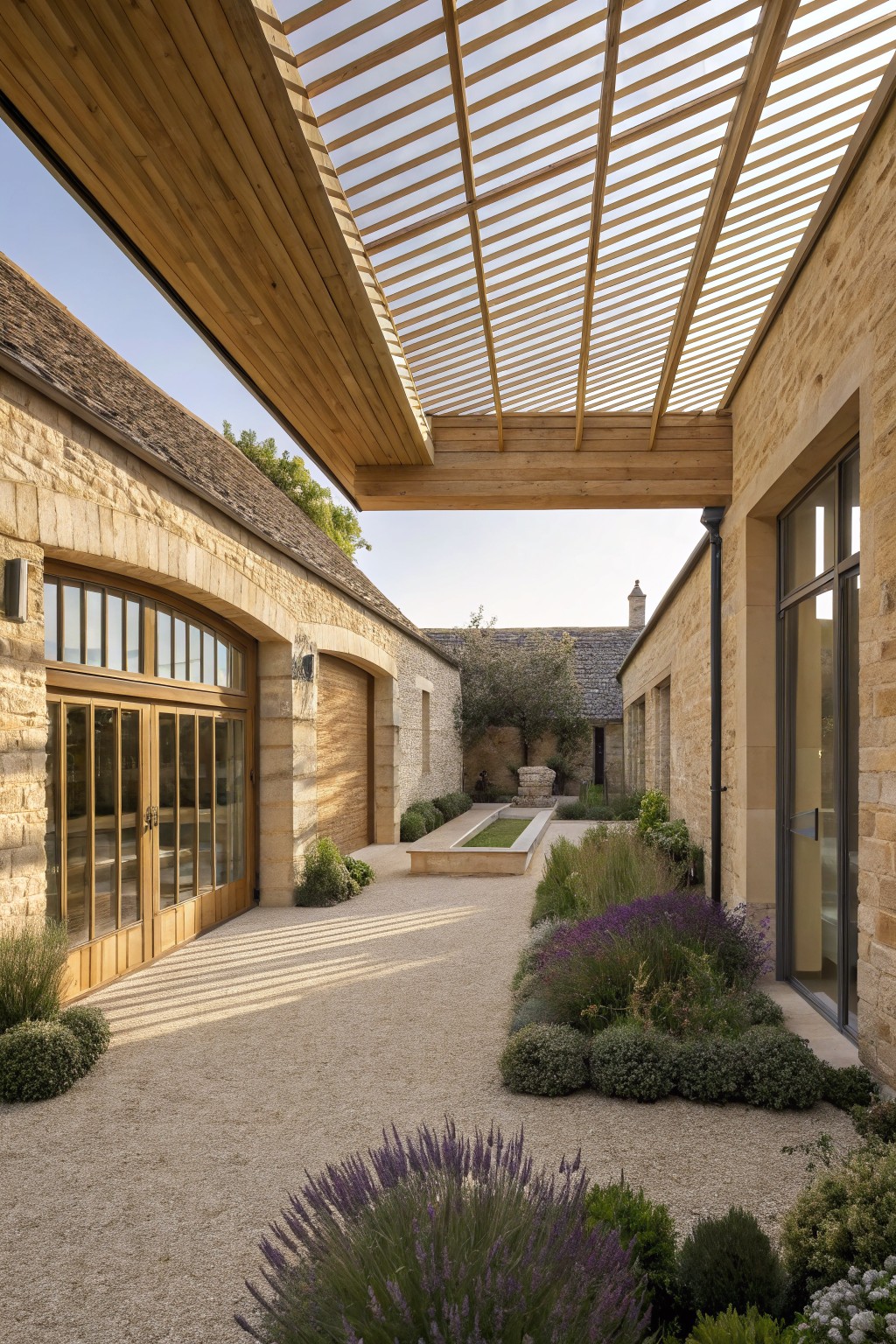 Courtyard between two stone buildings with a wooden slatted roof overhead, gravel ground, and scattered plants.
