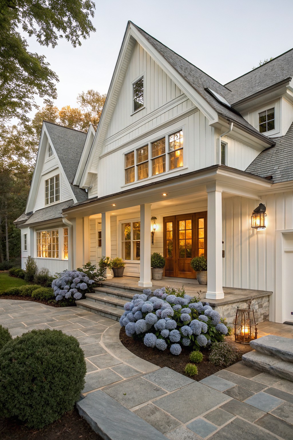 A white traditional farmhouse exterior with a covered front porch supported by white columns, a central double wooden door entry, and stone steps leading up from a paved walkway.