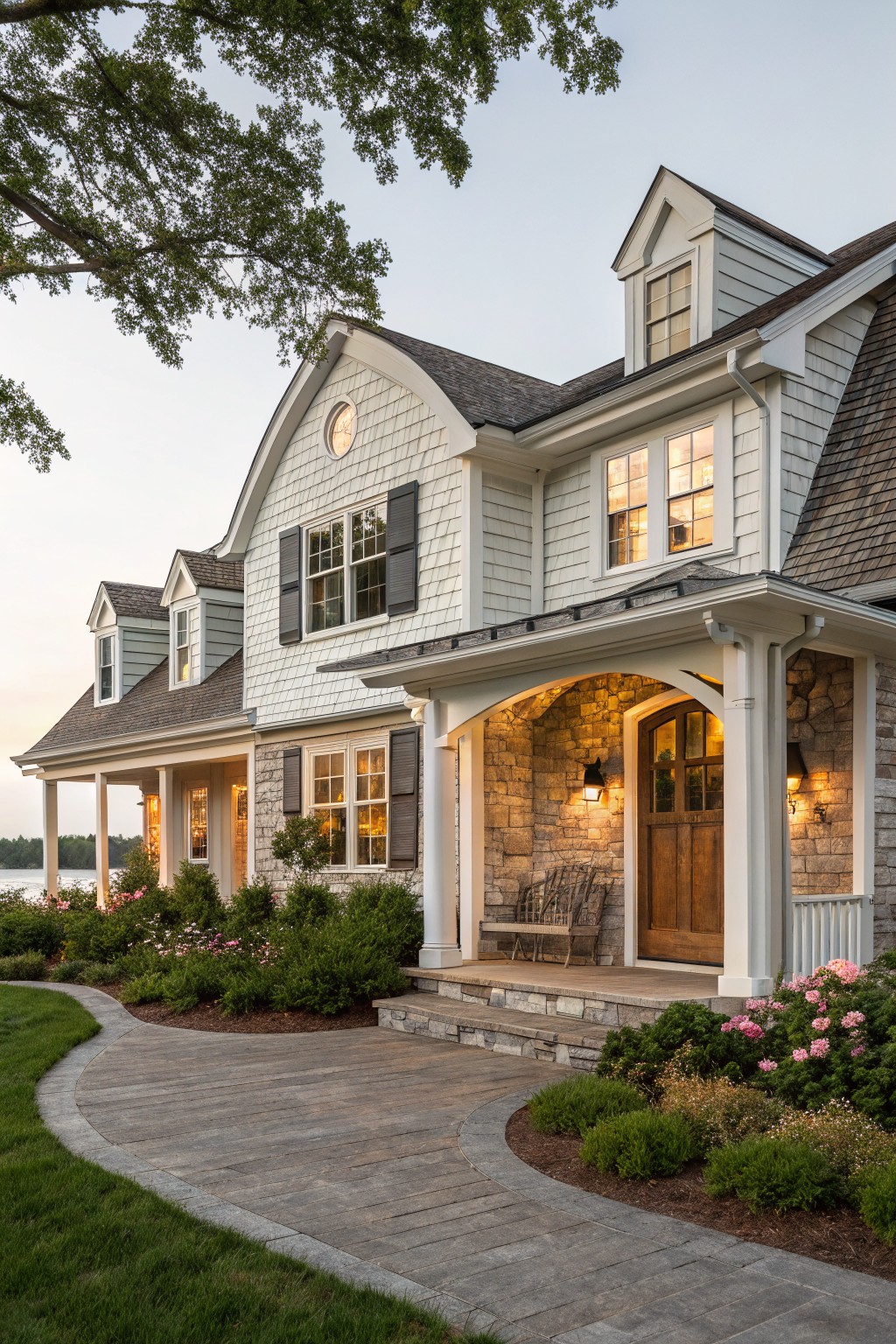 Large white house with stone porch, wooden door, and flower-lined path at dusk.
