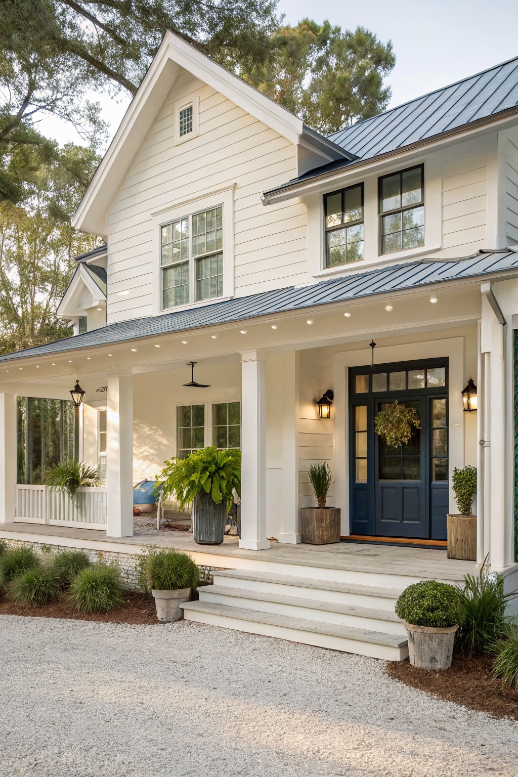 A white coastal farmhouse with horizontal siding, a navy blue front door, a covered porch with white columns, and a dark metal roof.