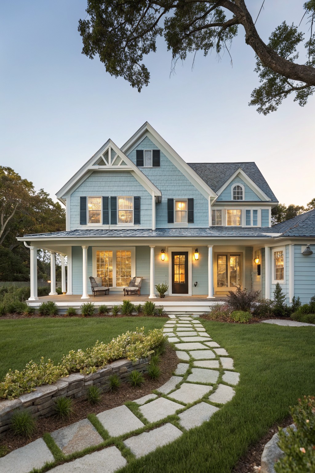 A two-story light blue house with white trim, a covered front porch, dark shutters, and a winding stone path through the lawn.