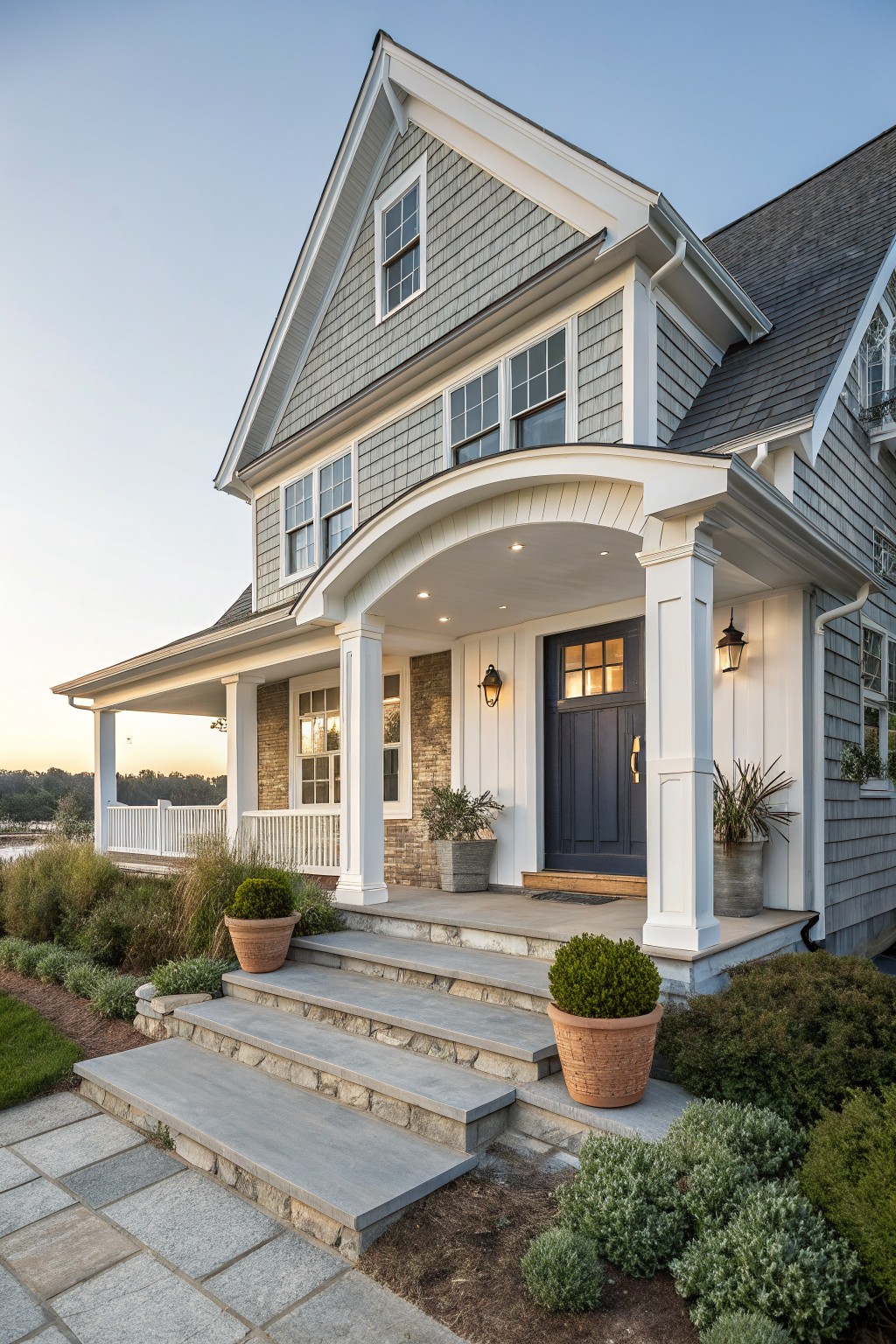 Gray shingled house with white arched porch, blue door, and stone steps.