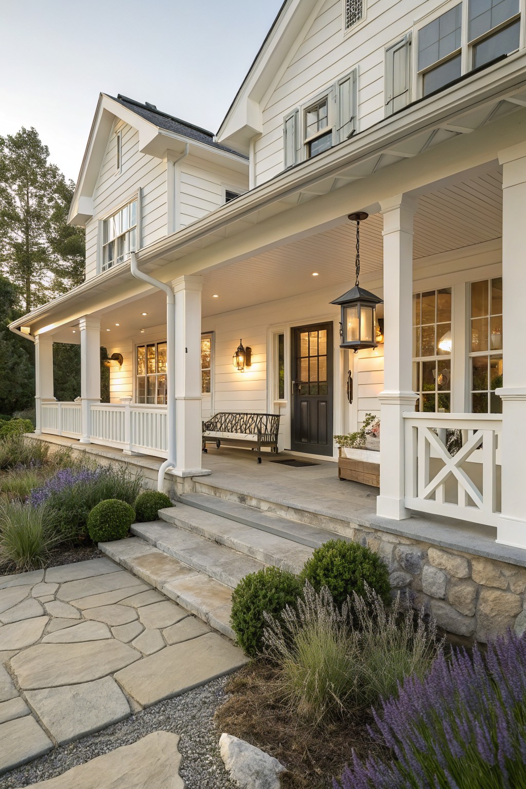 White coastal farmhouse exterior with dark front door, covered porch, stone foundation, and surrounding landscaping.