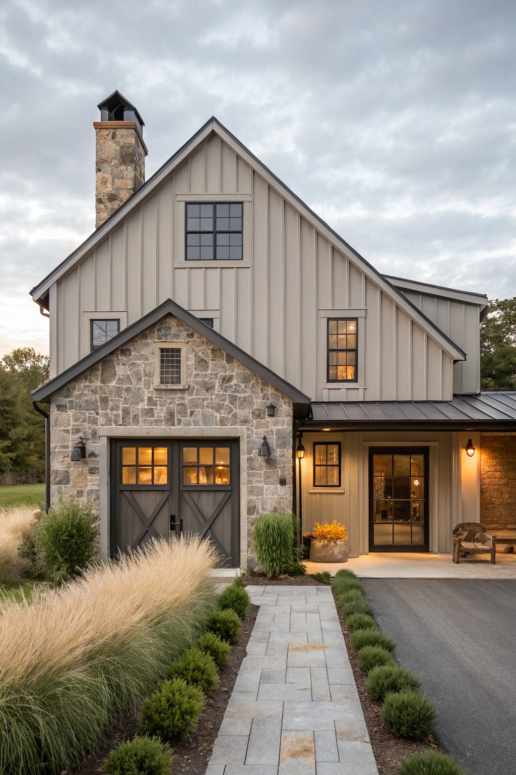 A two-story farmhouse exterior with stone on the lower portion and soft gray siding above, including a dark-trimmed garage and chimney.