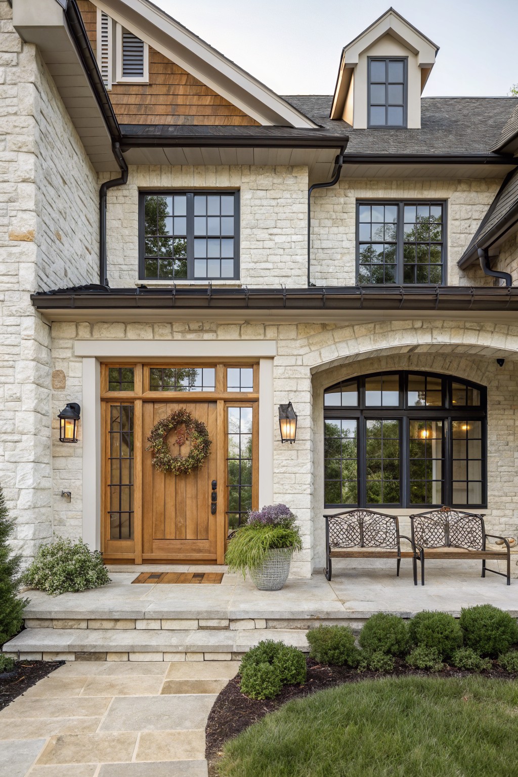 Stone house exterior featuring a wooden front door with sidelights, an arched window section, and two benches on the porch.