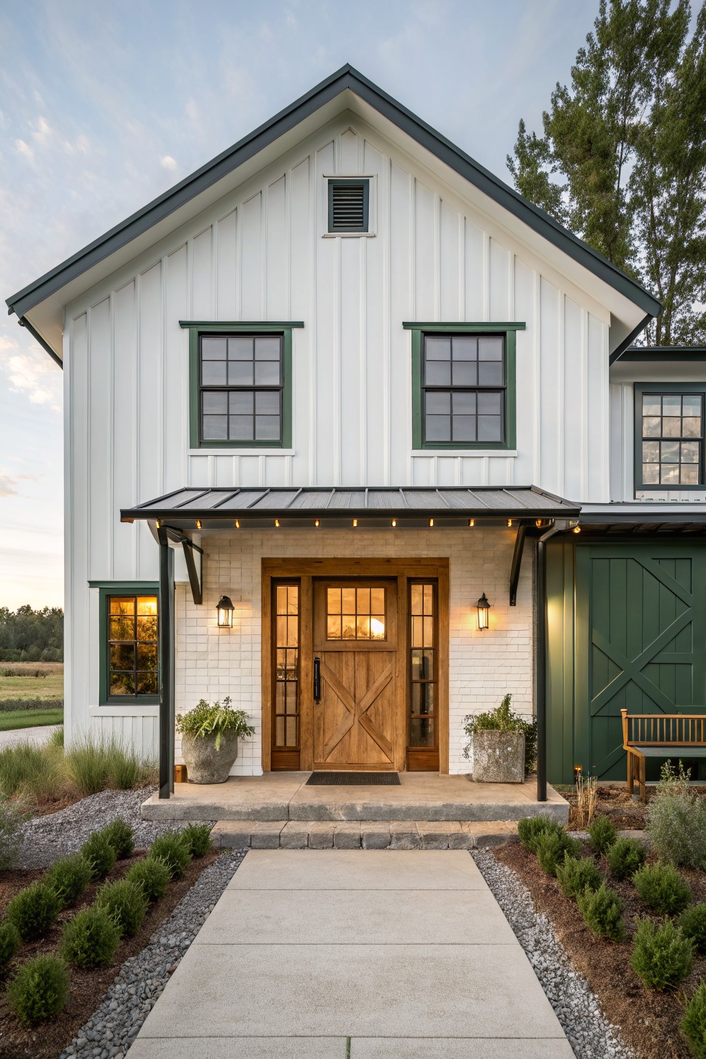 White farmhouse exterior with green trim, centered wood entry door under a metal awning with string lights, and stone base at the entry.