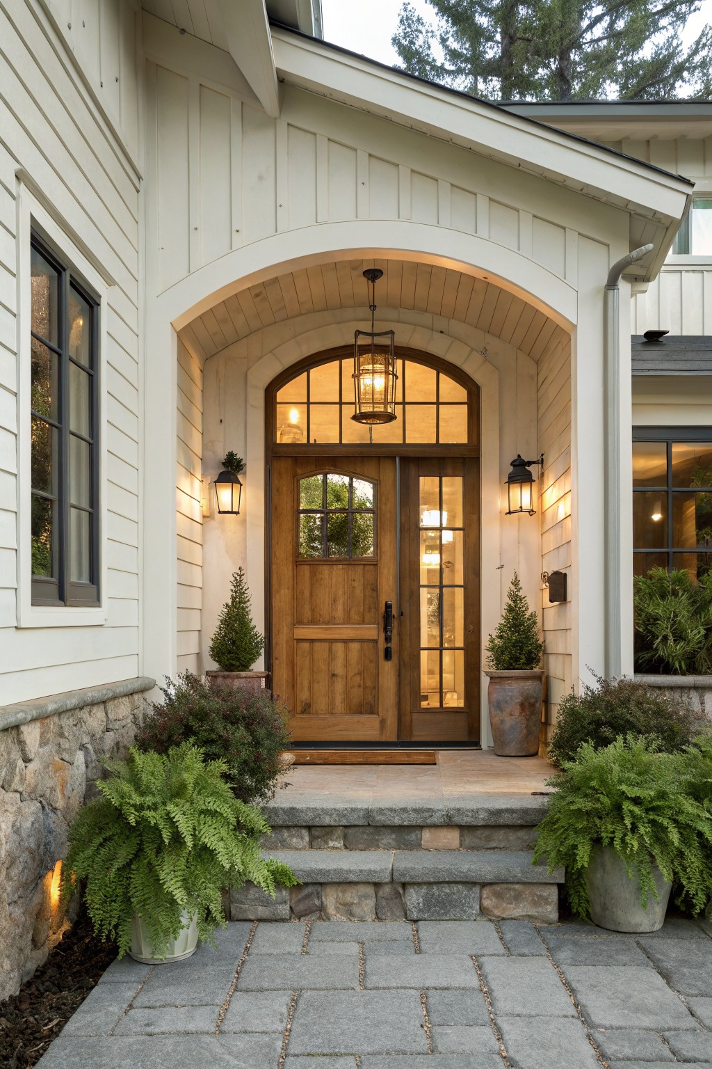 Arched wooden double doors at house entrance with potted ferns and lanterns