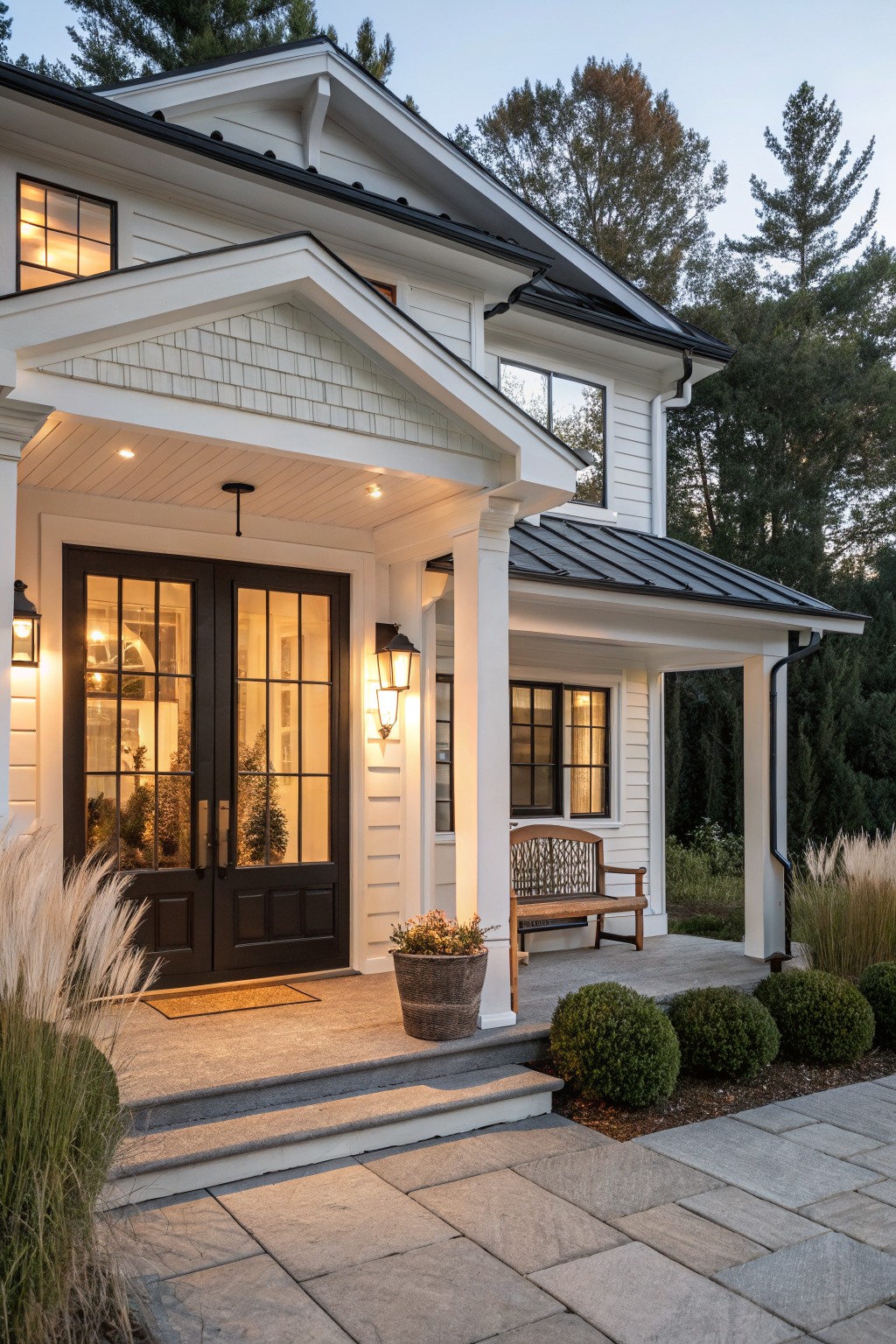 A white farmhouse exterior with a covered porch, dark double entry doors framed by white trim, a wooden bench, and stone steps.