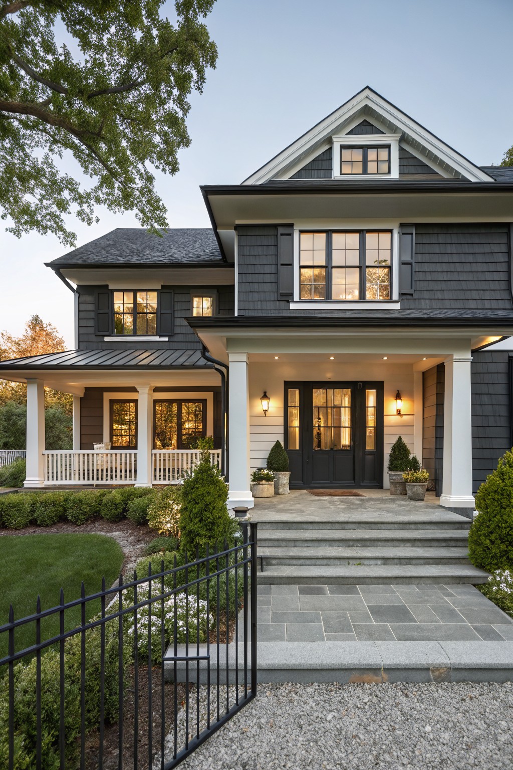 A two-story house with dark gray shingle siding, white trim, a covered porch with white columns, and a black front door.