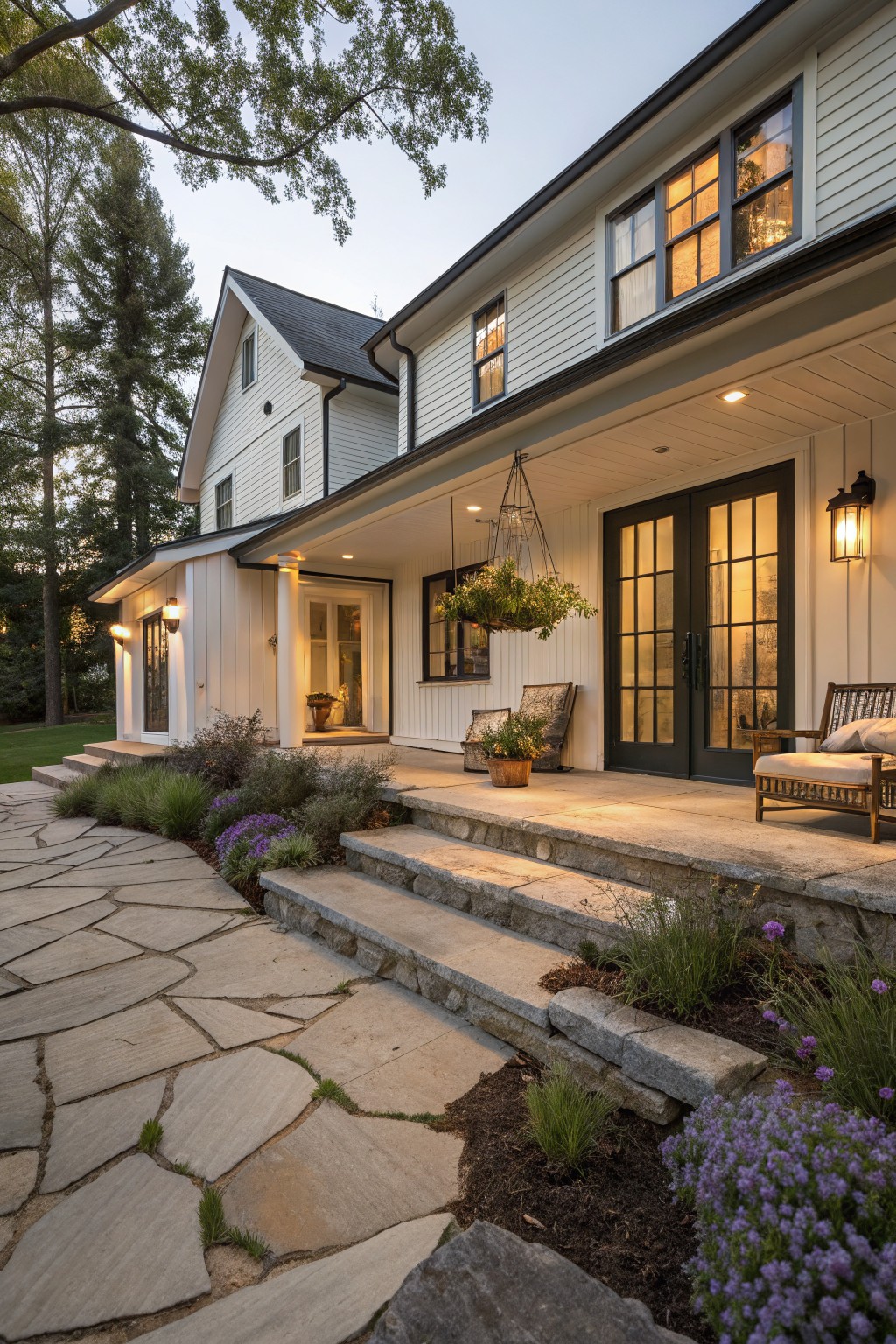 White house with stone steps, porch lights, hanging plants, and flagstone path at dusk.