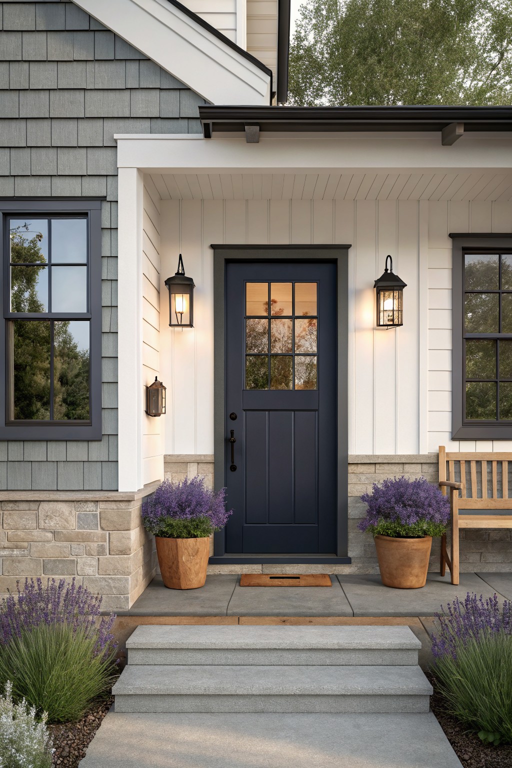 Front view of a house entry featuring a dark navy door with black trim, white siding, two black lanterns, and potted plants on either side of the steps.