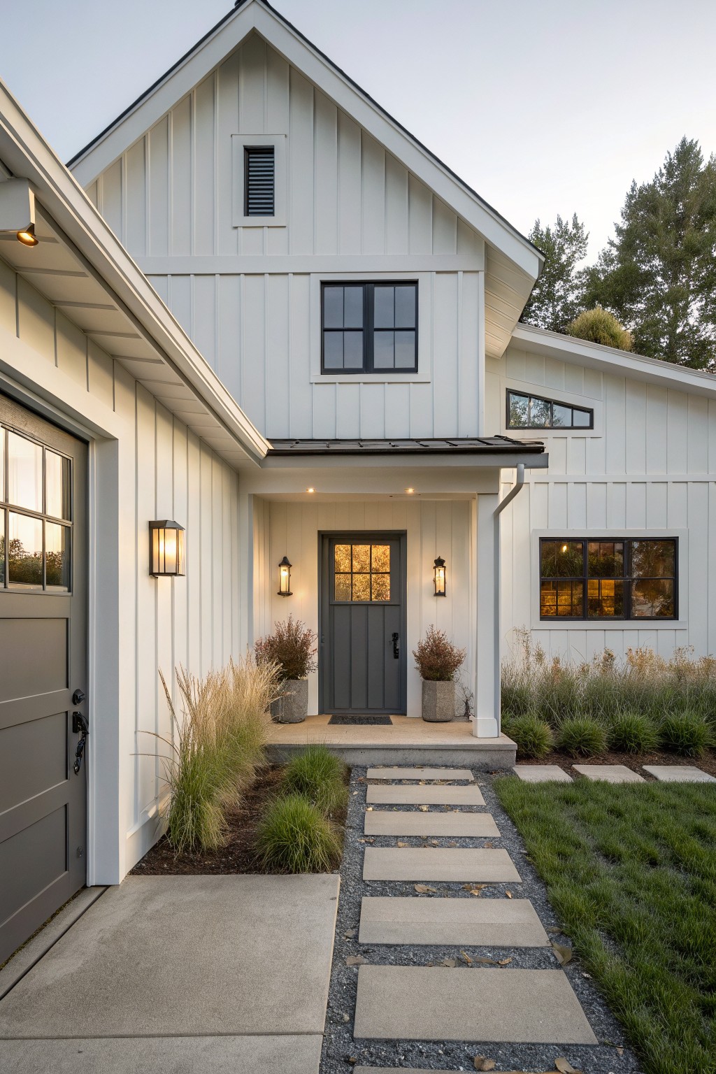 Front view of a white farmhouse with vertical siding, a dark gray door, black window frames, and a concrete pathway with stepping stones.