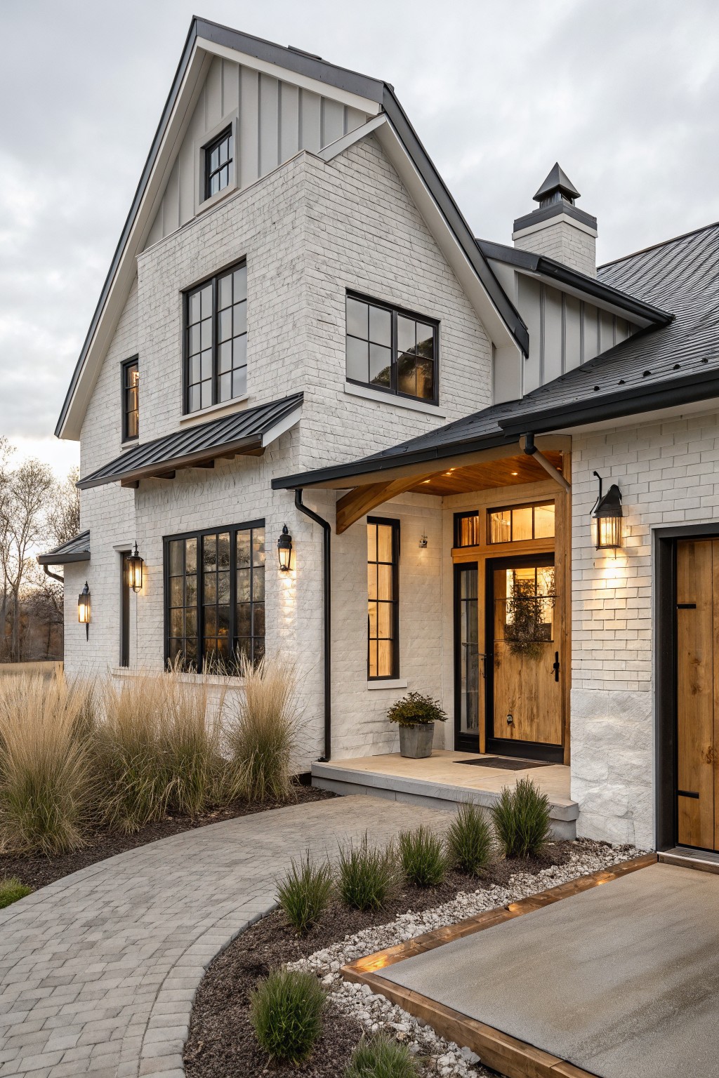 Front view of a white brick farmhouse with black metal roofing, black-framed windows, and wooden front doors.