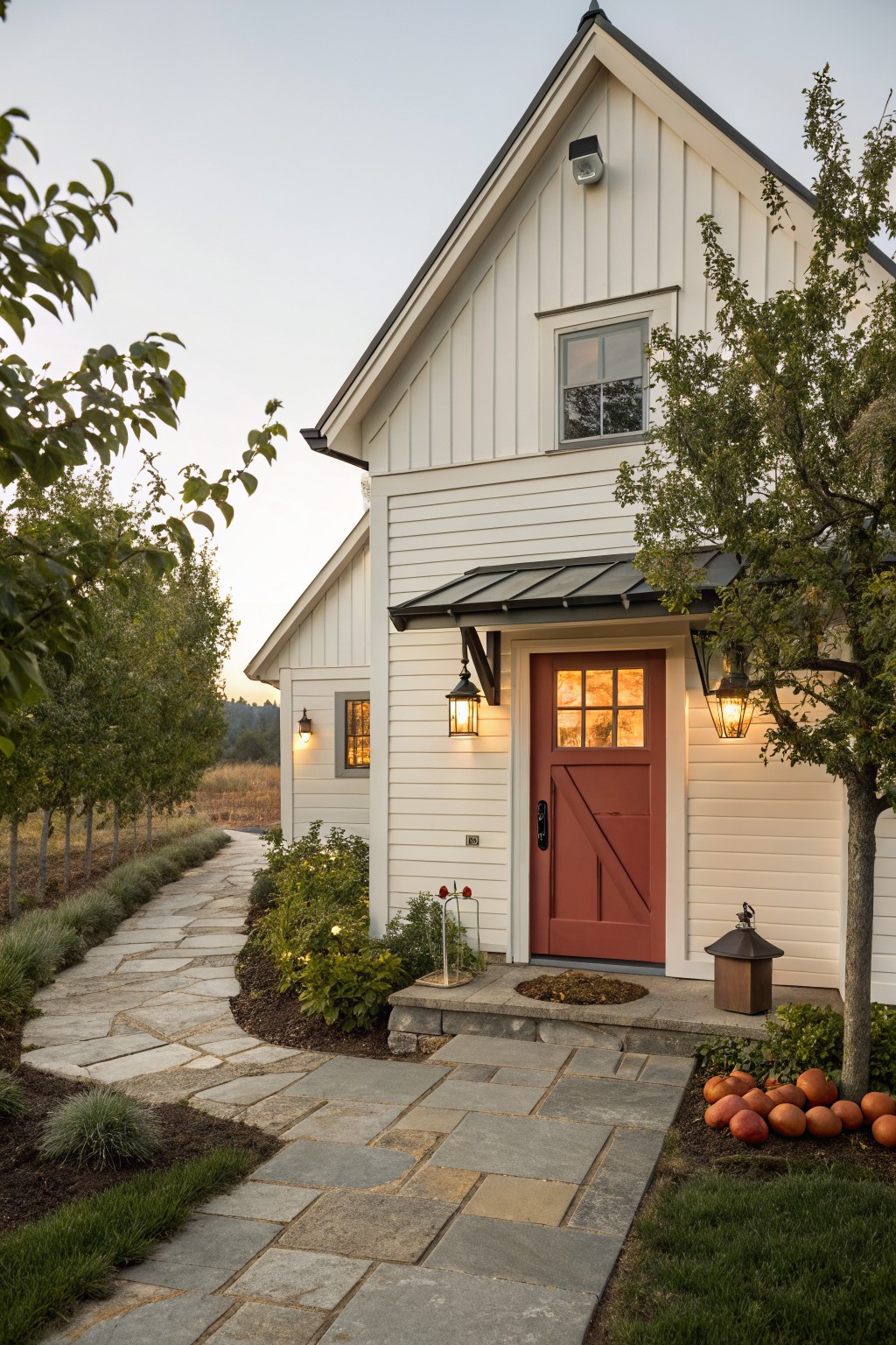White farmhouse exterior with vertical siding, a red door under a small metal awning, stone pathway, and trees on the right.