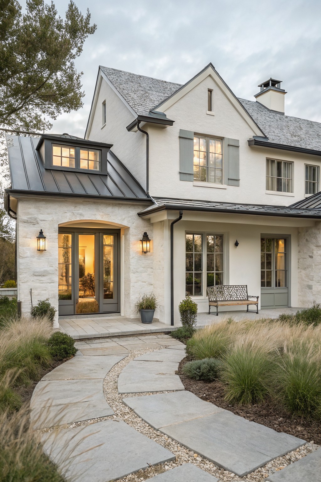 A white farmhouse exterior with gray shutters, an arched entry with double doors, stone accents, and a curving stone pathway.