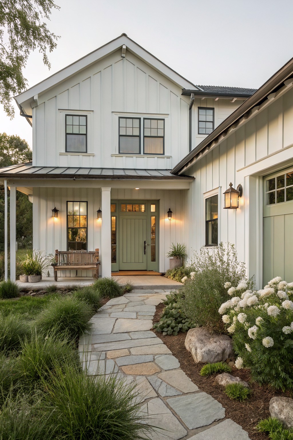 A white farmhouse with vertical siding, a sage green front door, black window frames, and a stone path leading to the porch.