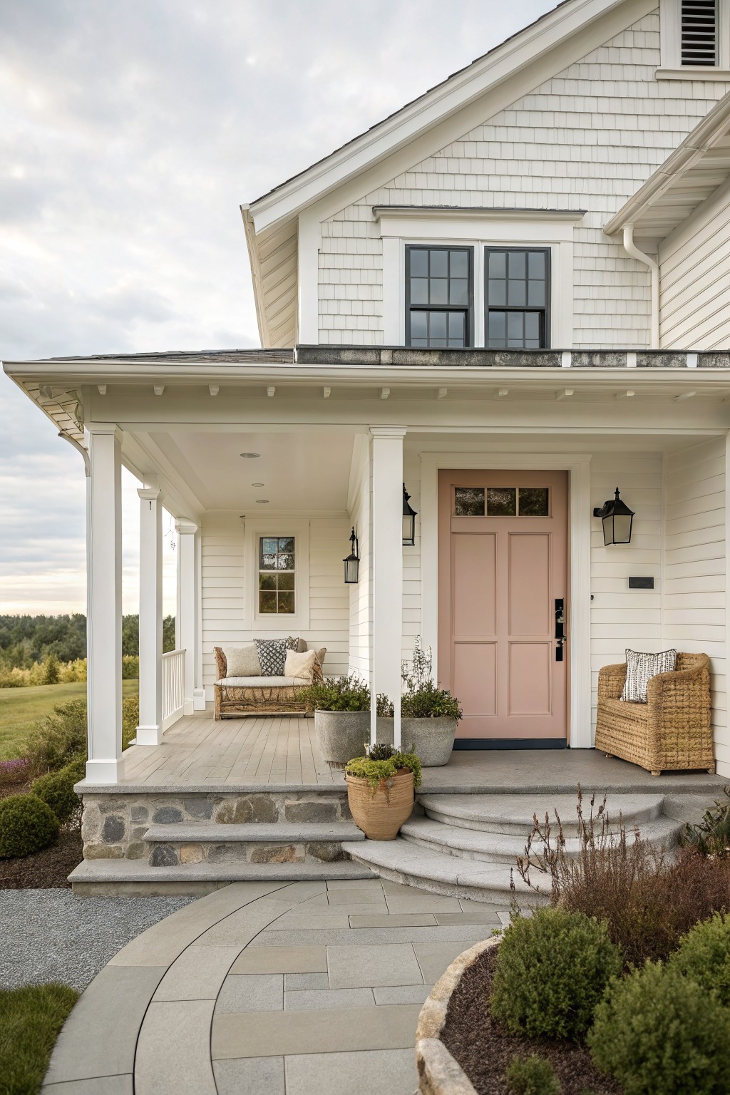 A white shingled farmhouse with a soft pink front door, white porch columns, and stone steps.