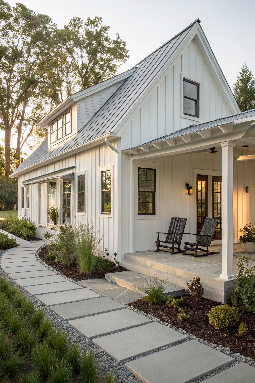 A white farmhouse exterior with vertical siding, a gabled metal roof, a front porch with two rocking chairs, and a stone pathway along the side.