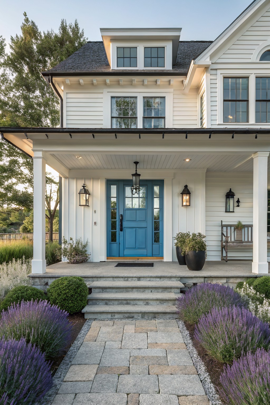 A white two-story farmhouse with a bright blue front door, covered porch, and stone pathway lined with purple flowers.