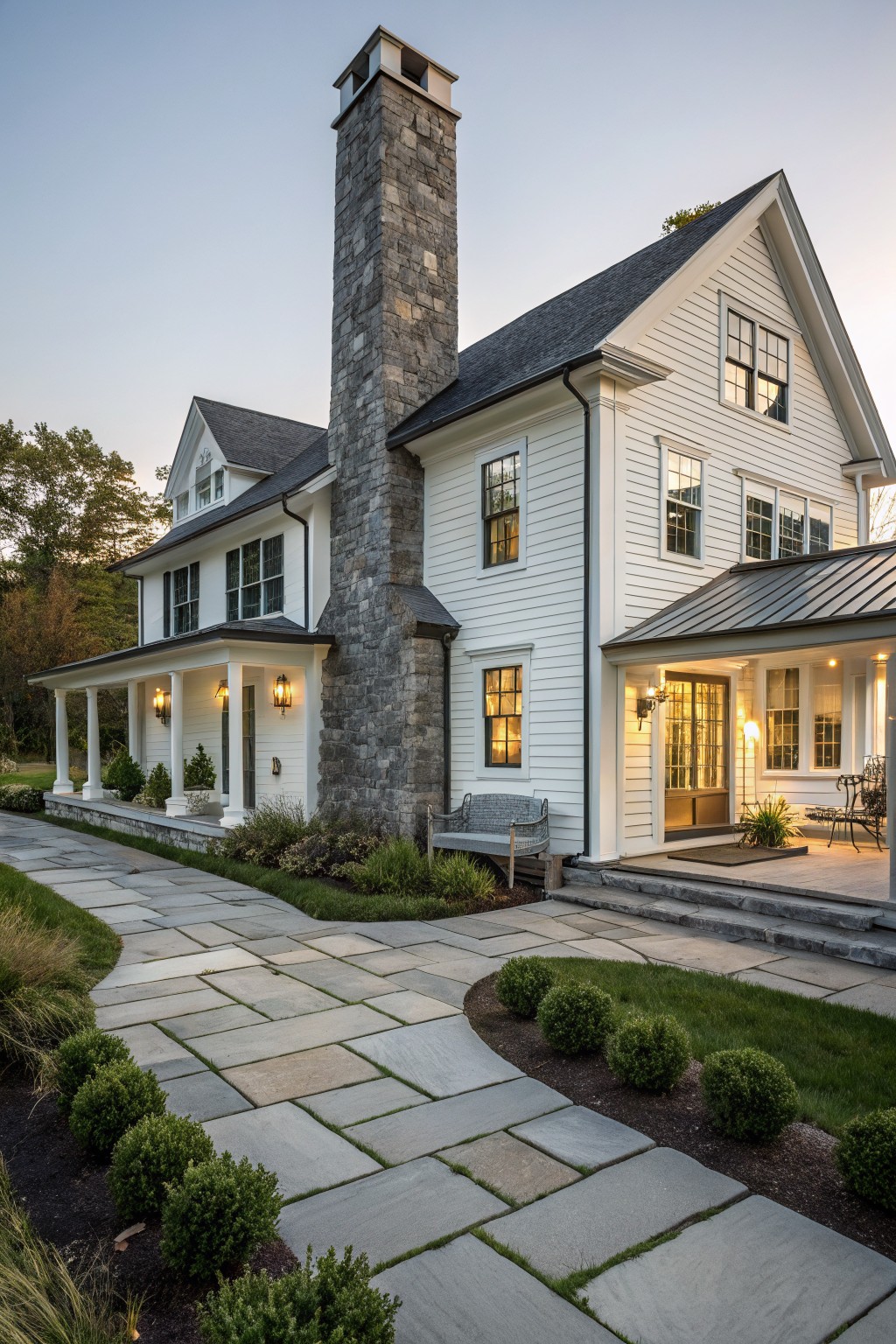 A white two-story farmhouse with a tall stone chimney, dark roof, front porch, and stone pathway.