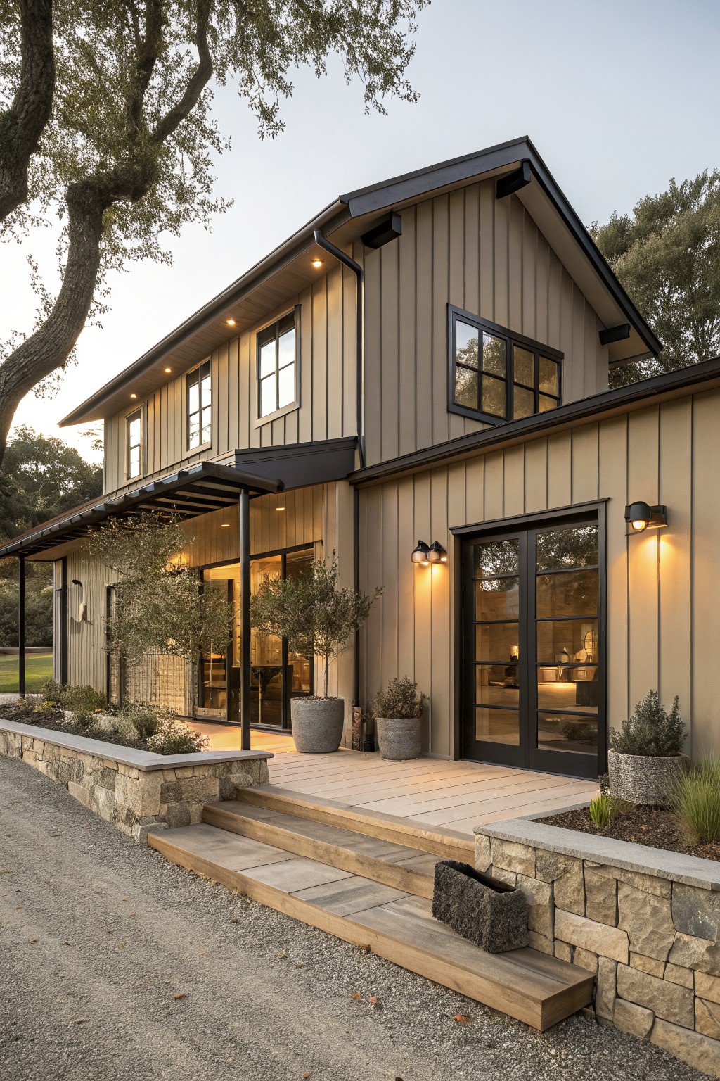 A two-story house with taupe board and batten siding, black window and door trim, and a wooden front deck with stone landscaping.