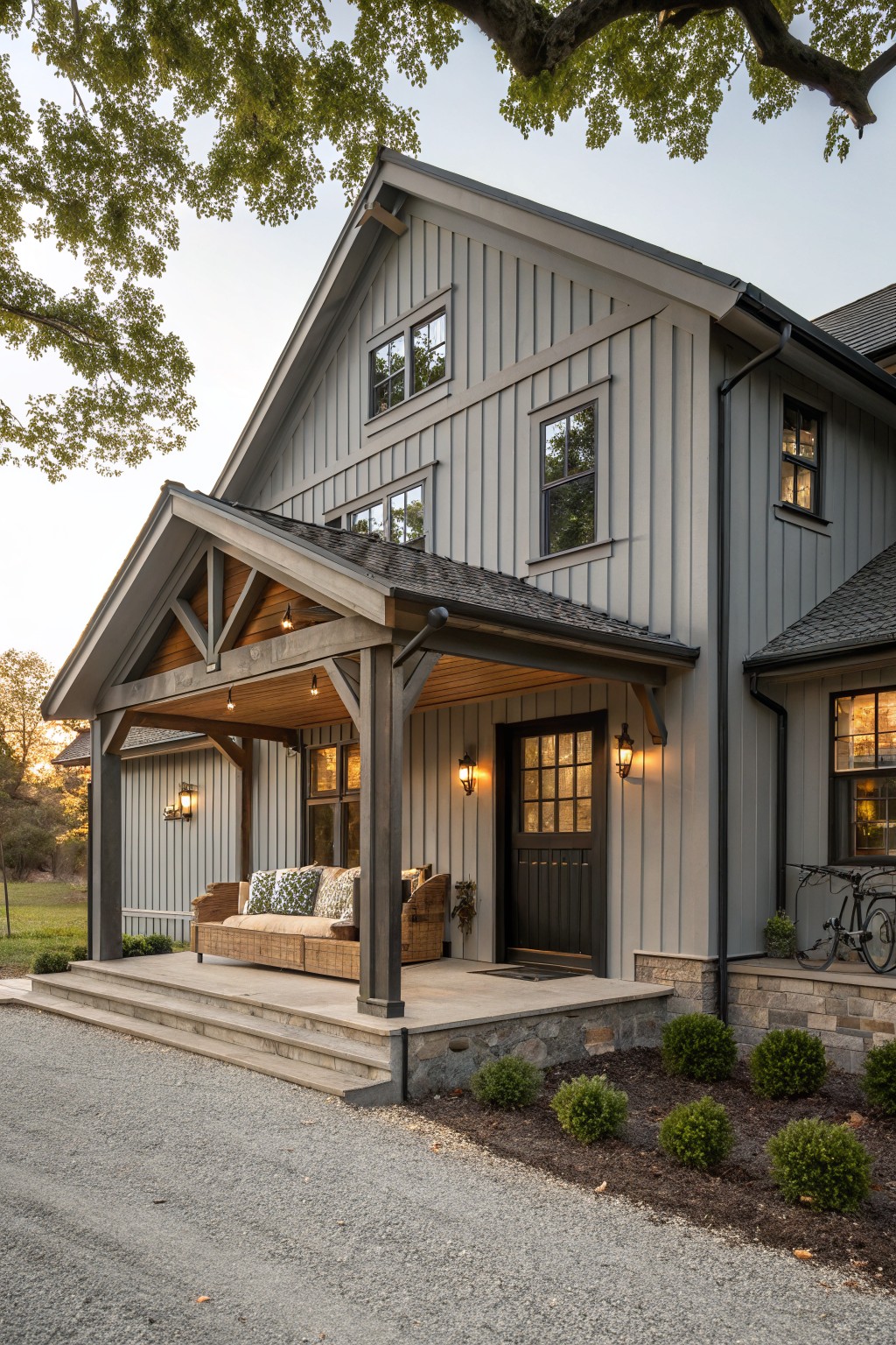 A gray board and batten farmhouse with a gabled porch, dark door, and stone foundation at the entry.