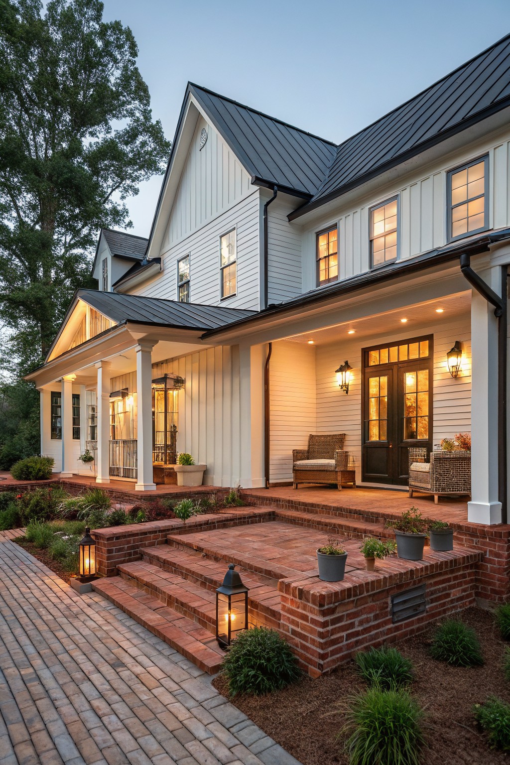 A white two-story farmhouse with board and batten siding, a black metal roof, brick steps and foundation, and a covered front porch with seating.