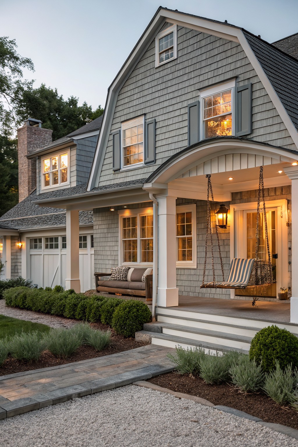 Gray house with white trim, lit windows, and striped hanging porch swing.