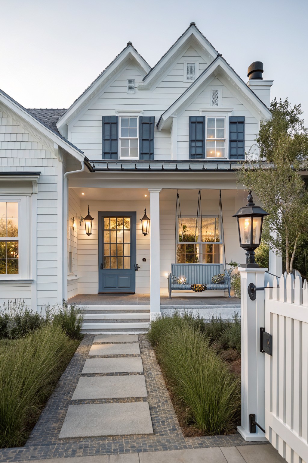 White house with blue door, porch swing, lanterns, and stone pathway at dusk