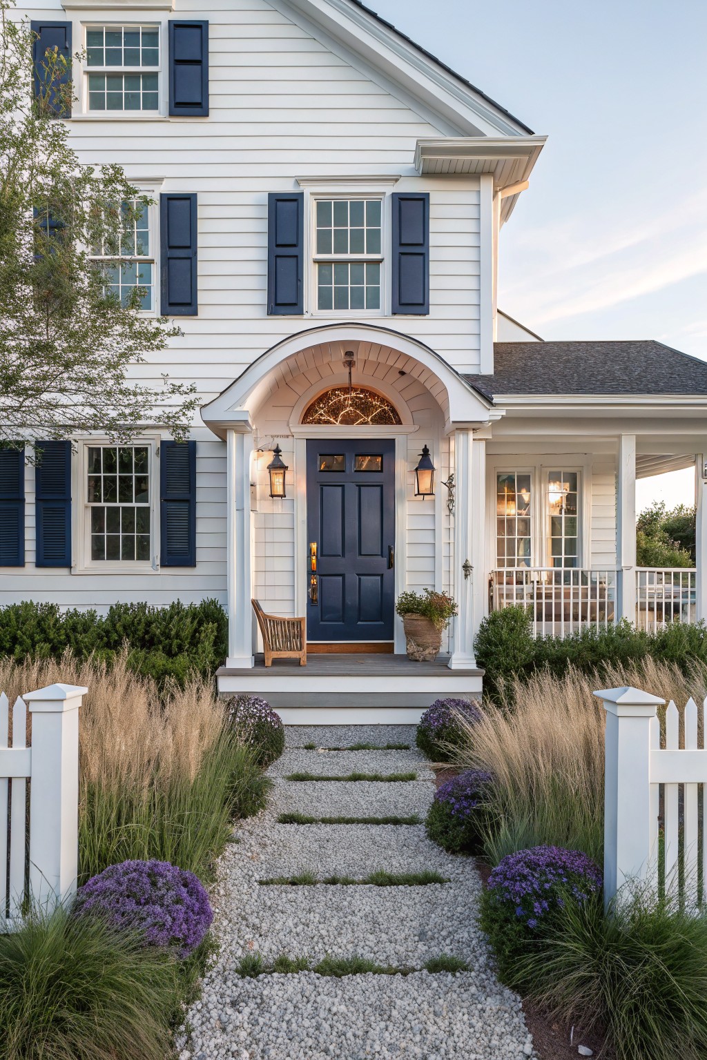 White house with navy shutters and door, gravel path through flowering garden to porch
