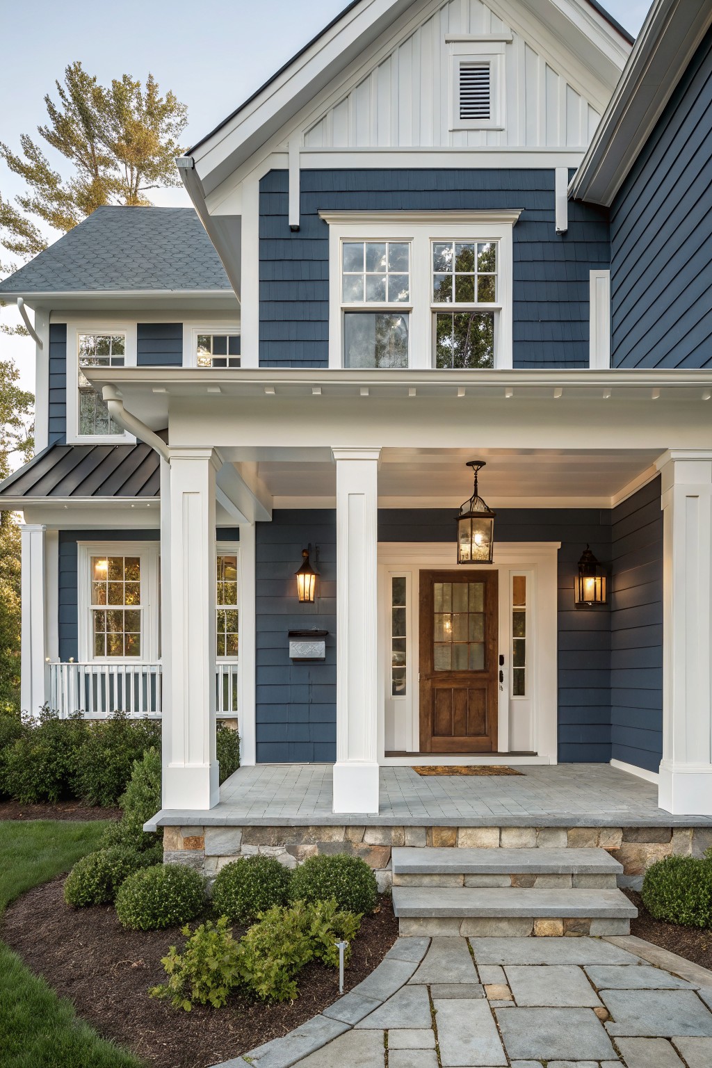 A two-story house with dark blue siding, white trim and columns, a covered porch, and stone steps leading to a wooden front door.