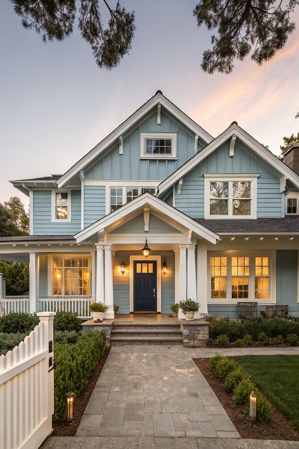 A two-story light blue house with white trim, a central gabled porch supported by white columns, and a dark blue front door.
