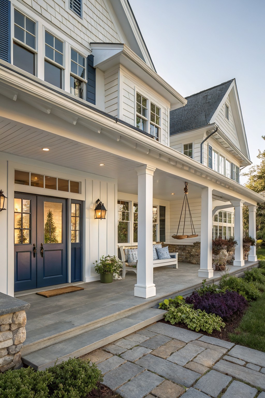 A white coastal farmhouse exterior with navy blue double doors, white columns on the porch, and a stone pathway leading to the entry.