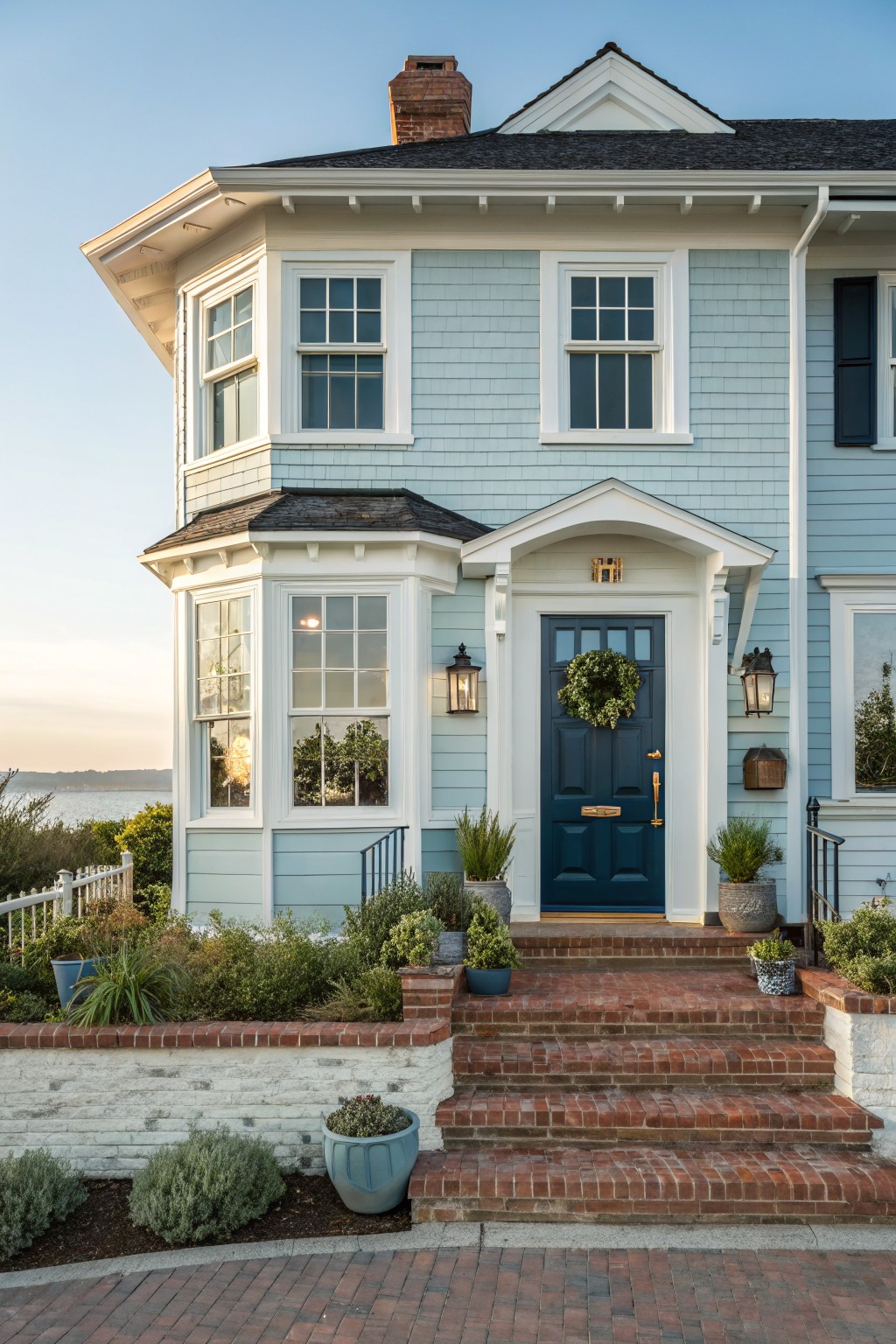 Front view of a two-story house with light blue shingle siding, white trim, a dark blue door, and brick steps.