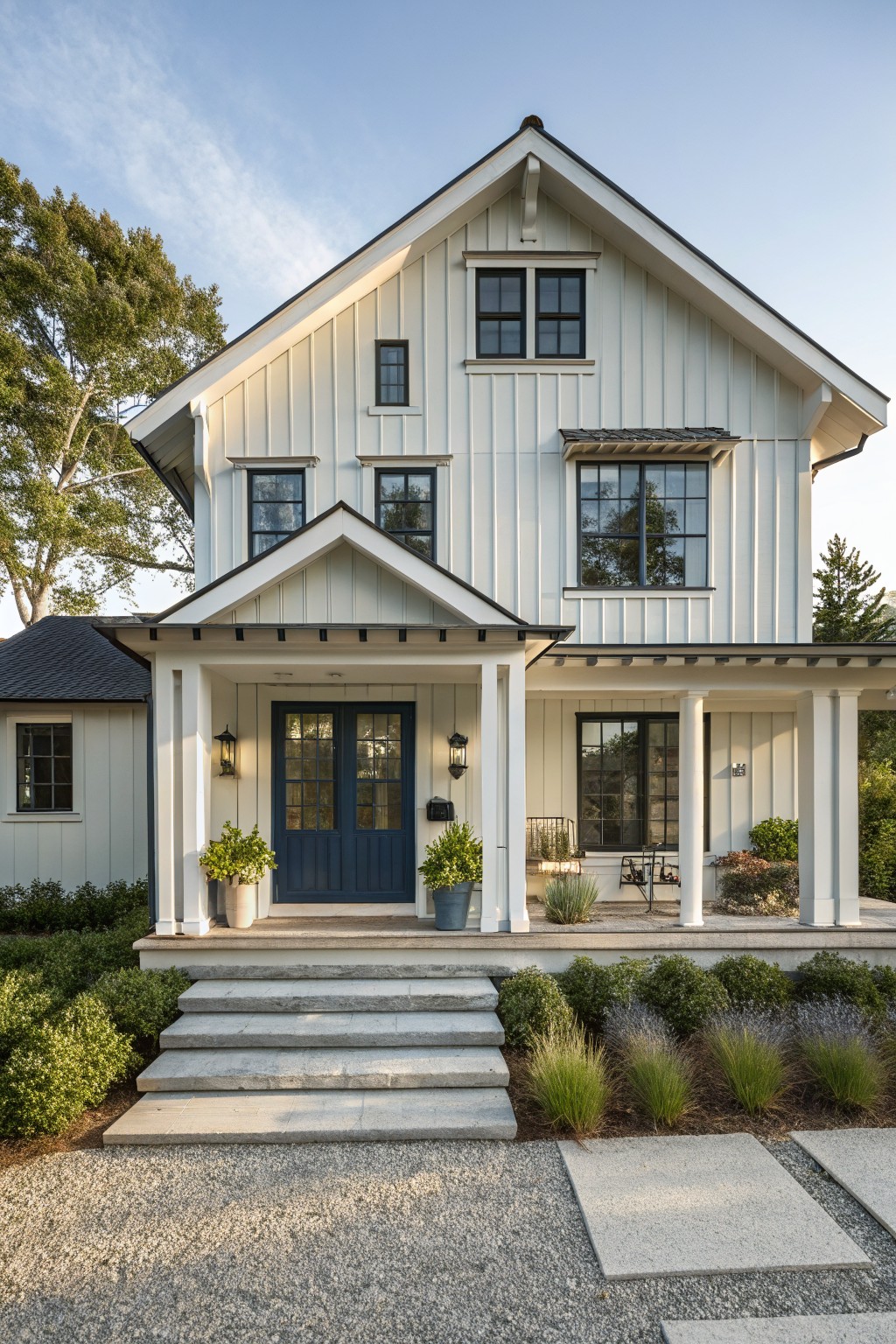 White two-story house with blue door, porch columns, stone steps, and garden.