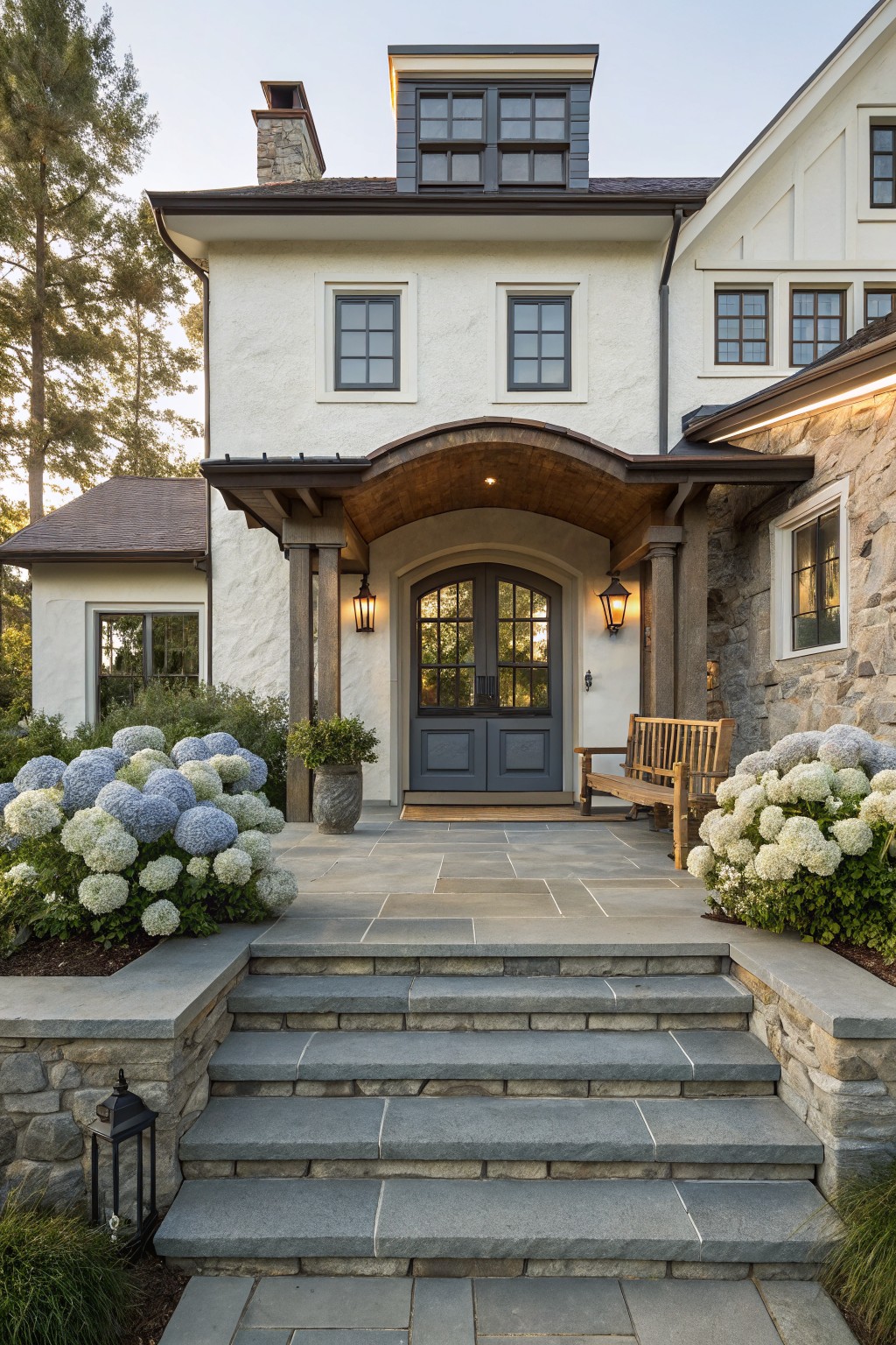 Front view of a two-story white house with an arched wooden portico over double gray doors, stone accents, and steps leading to a stone patio.
