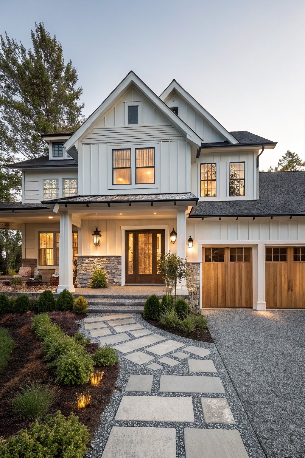 A white two-story house with gables, a covered entry porch with stone base, wood door, and a stone pathway on gravel leading to the front steps, with wooden garage doors visible on the right side.