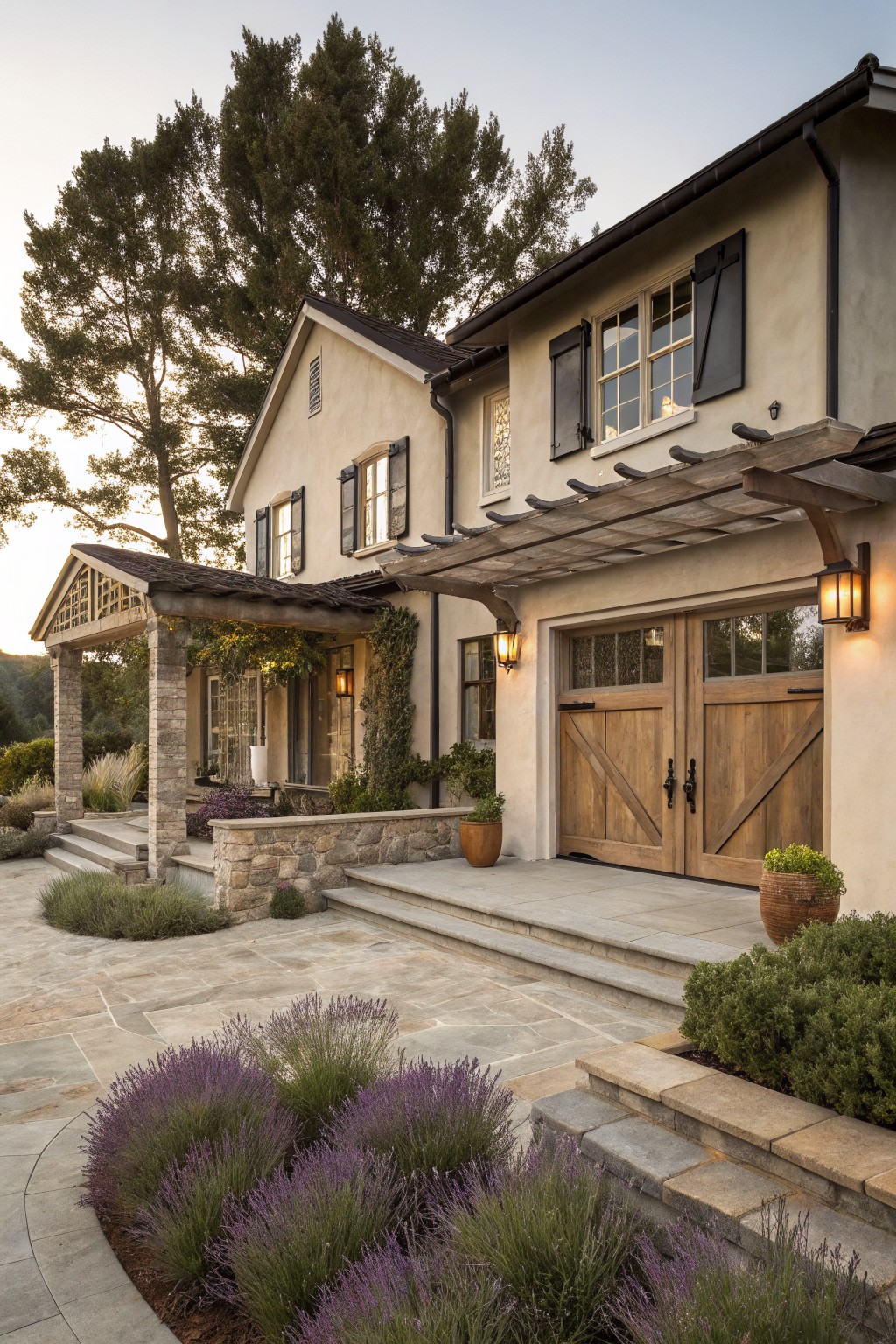 A front view of a one-story stucco house with wooden garage doors, black shutters, a wooden pergola covering the entry, stone accents, and purple flowering plants in the foreground.