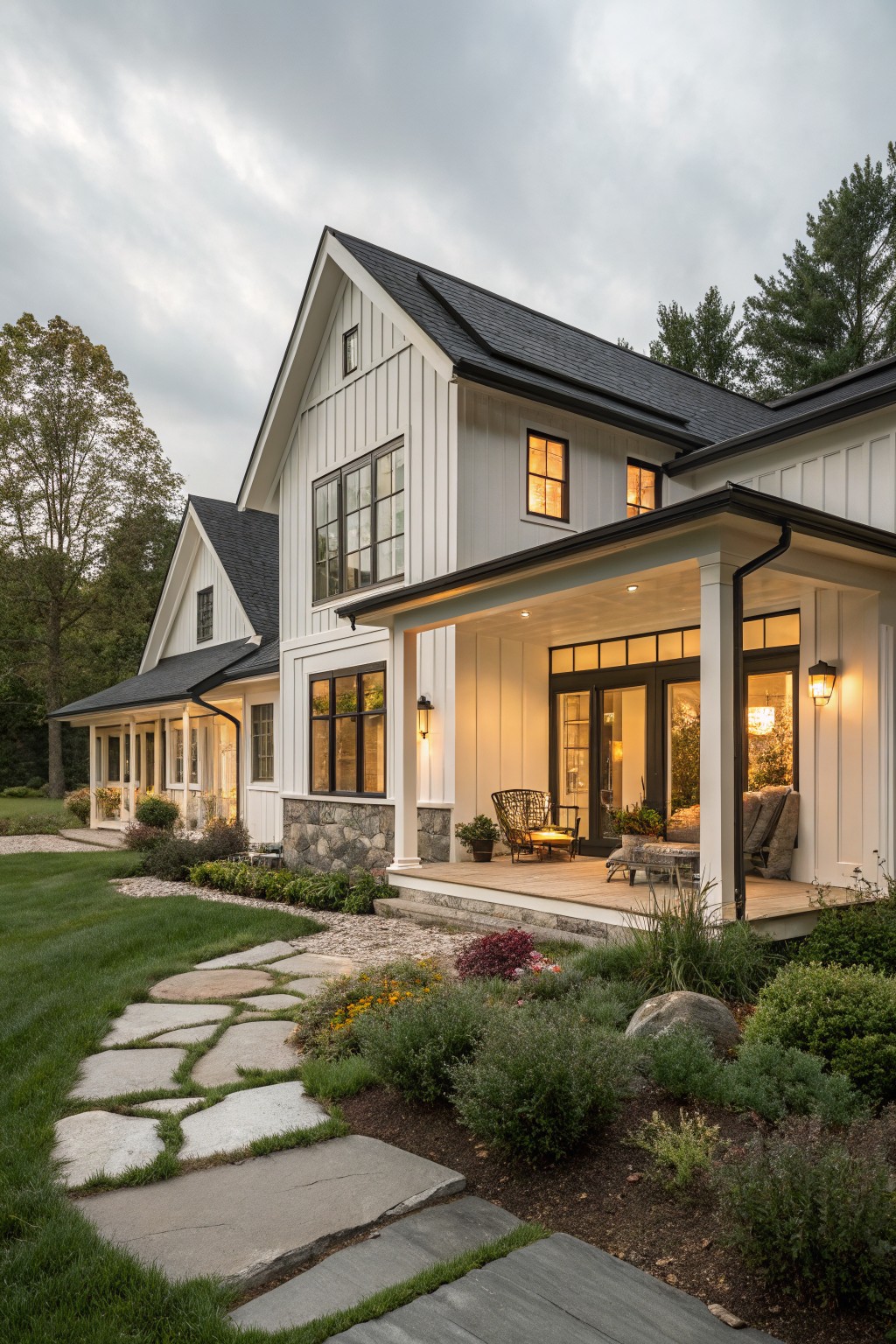White modern farmhouse with black roof, lit porch, and stone garden path