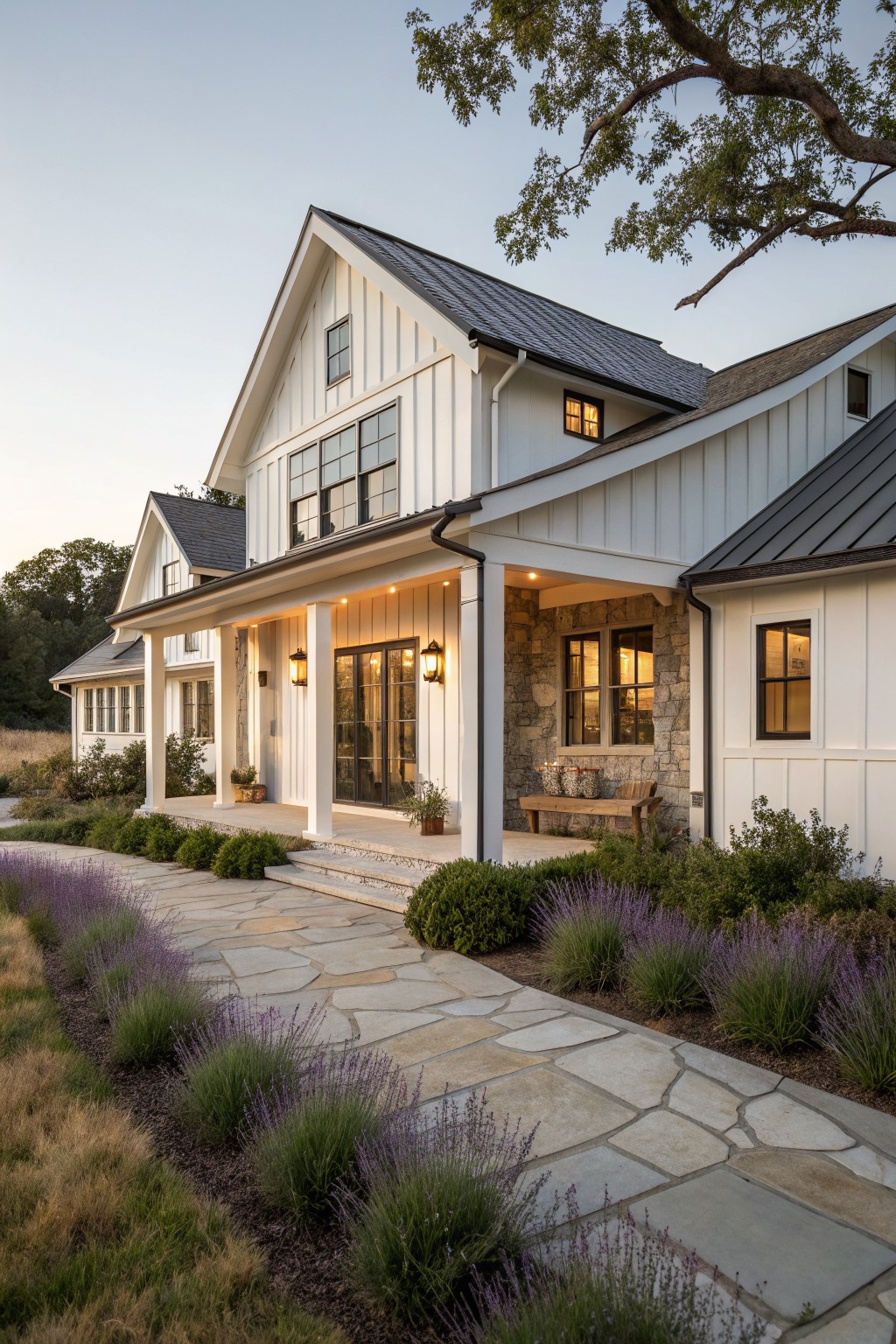 A white farmhouse exterior with stone veneer accents under the porch, a covered entry with columns, and a stone pathway bordered by lavender.