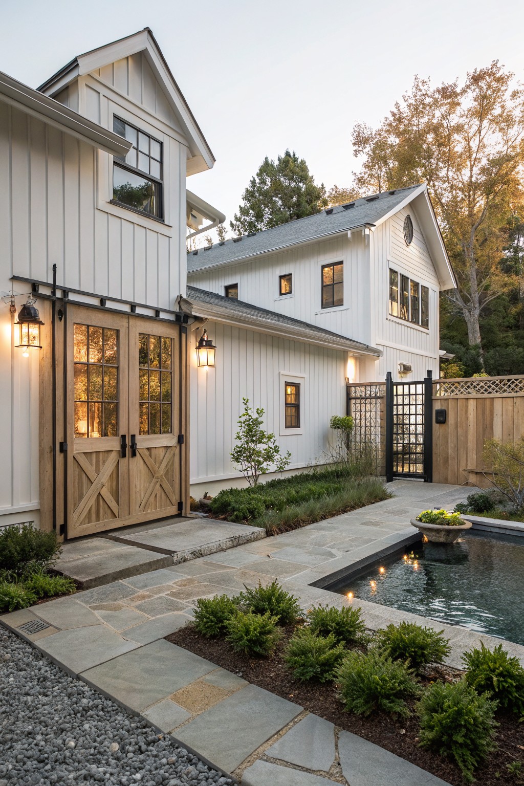 A white farmhouse exterior with large wooden barn doors, stone pathways, a small pool, and surrounding landscaping.