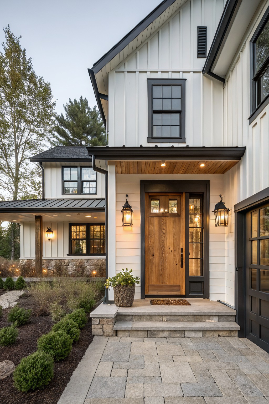 A white board and batten house with a centered wood front door, black trim, and a stone paver walkway.