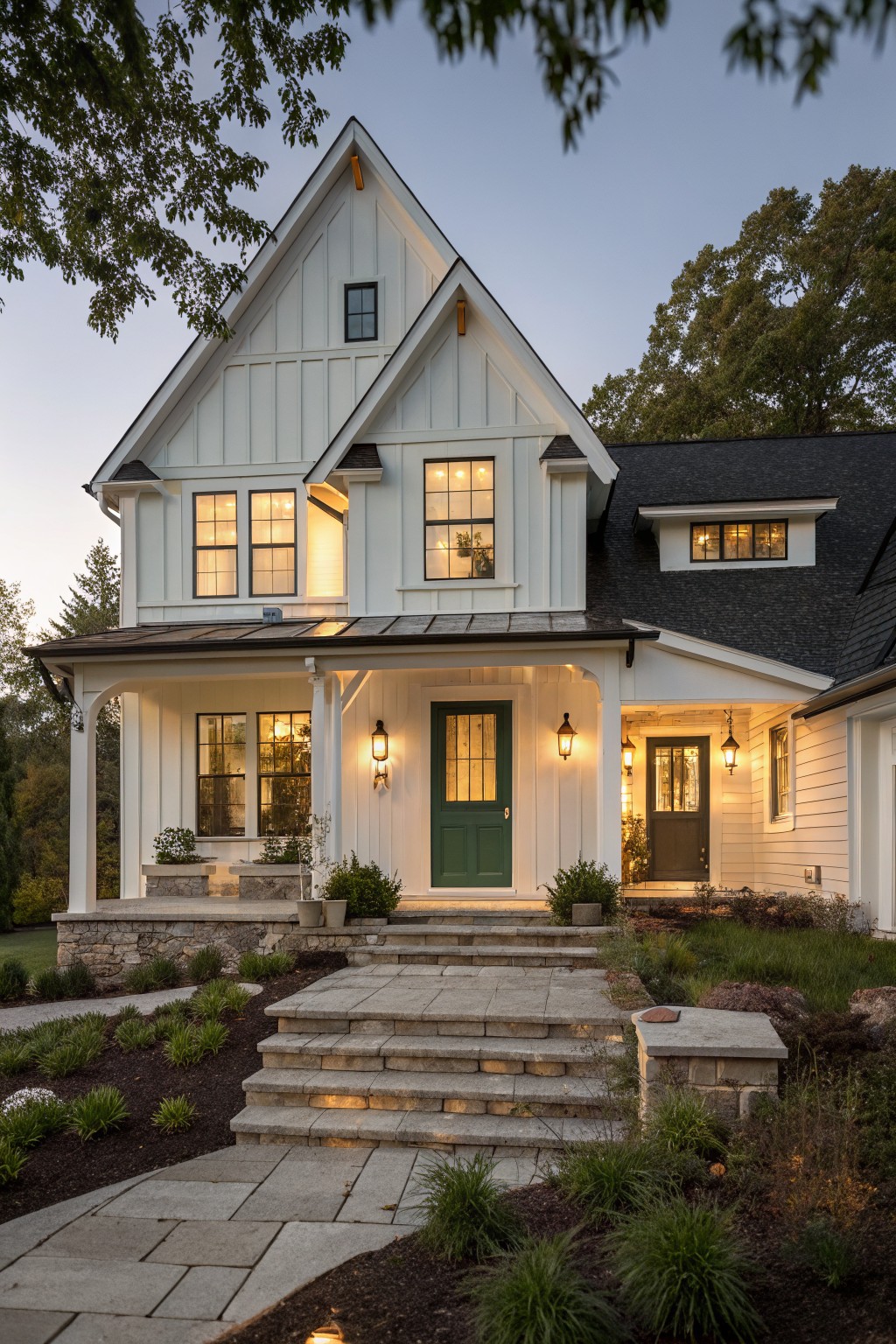 A white two-story farmhouse with board and batten siding on the front gables, a green door, and a covered stone porch at dusk.
