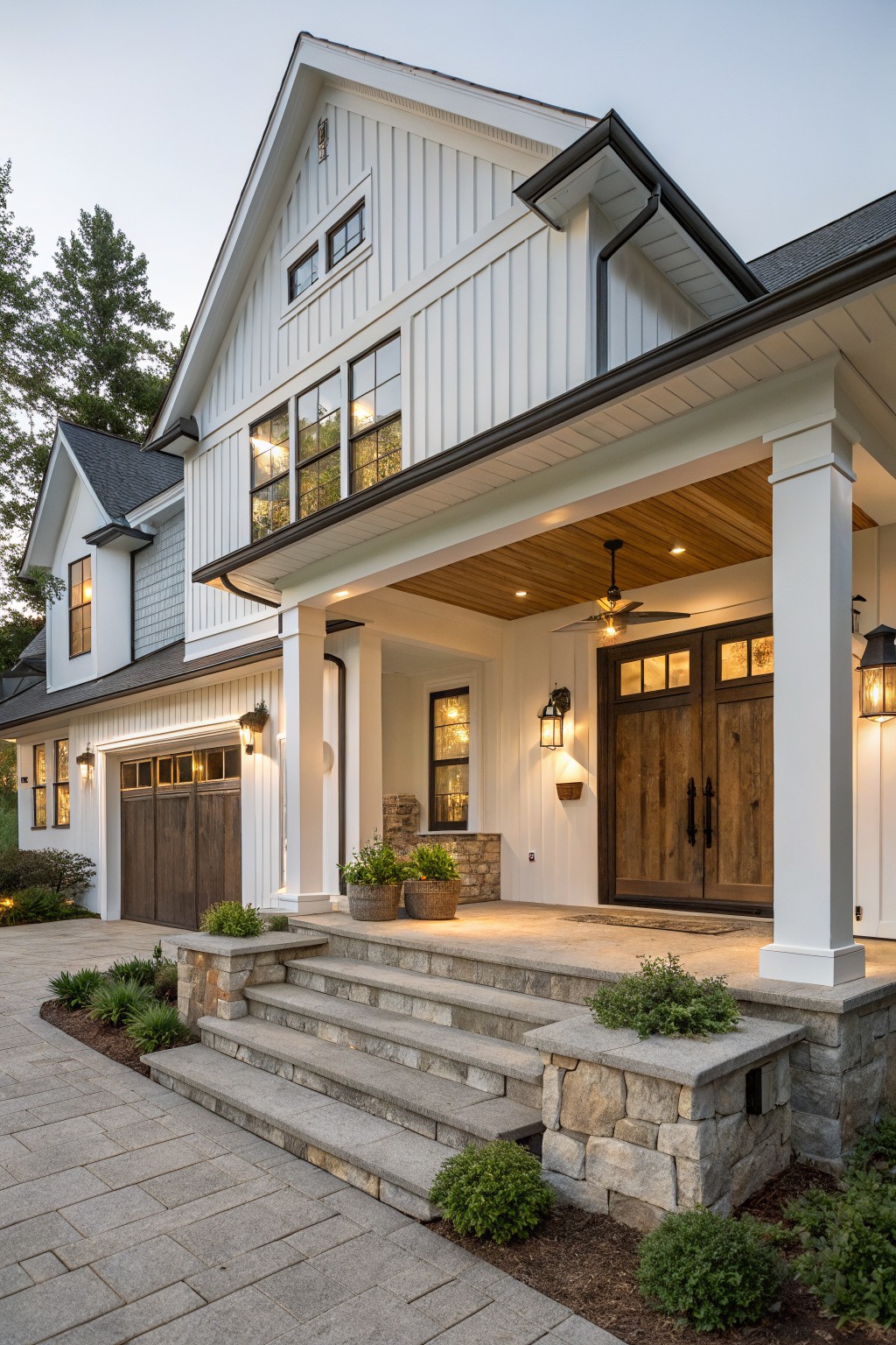 A white board and batten farmhouse with a covered porch, wooden double doors, stone steps, and a two-car garage on the left side.