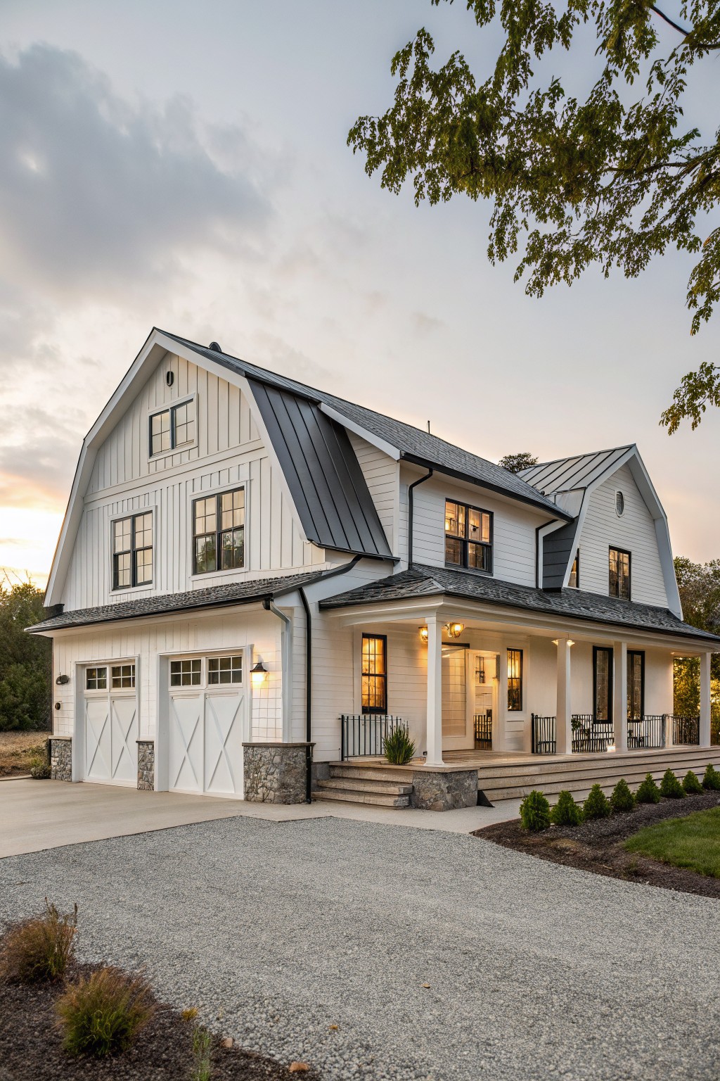 A large white two-story farmhouse with board and batten siding, multiple steep gables, black metal roofs, stone accents at the base, and a covered front porch.