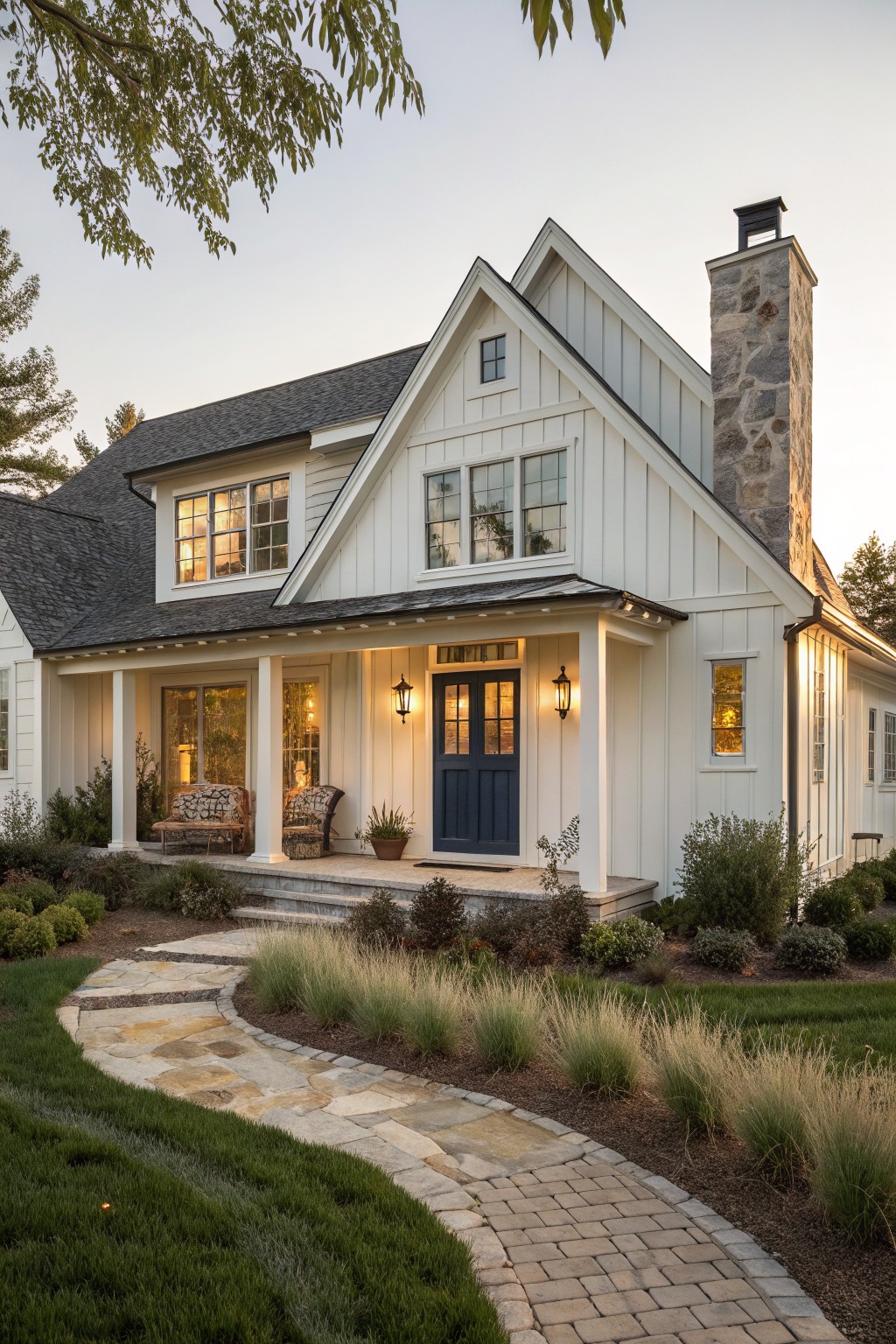 Front view of a white board and batten farmhouse with a navy blue front door, covered porch, and stone chimney.