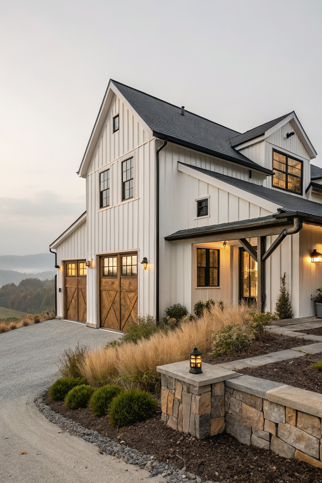 A two-story white farmhouse exterior with board and batten siding, black roof, wooden garage doors, and stone retaining wall in the foreground.
