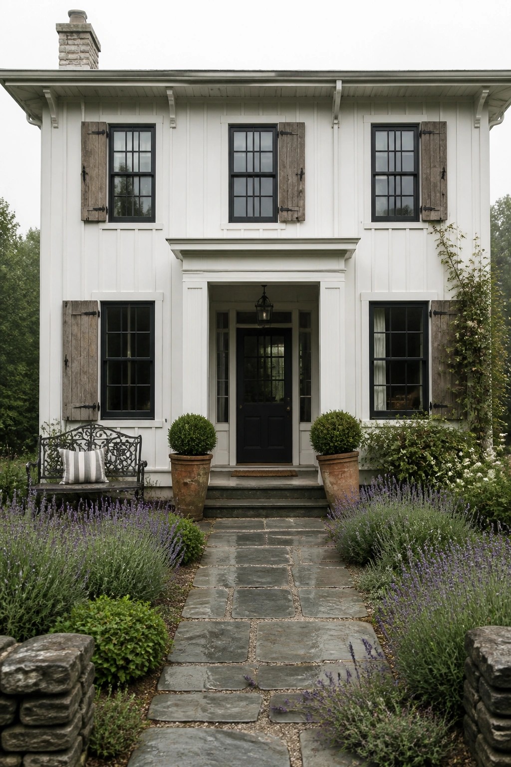A white two-story farmhouse exterior with black-framed windows, weathered wooden shutters, a centered black door, and a stone pathway leading to the entrance.