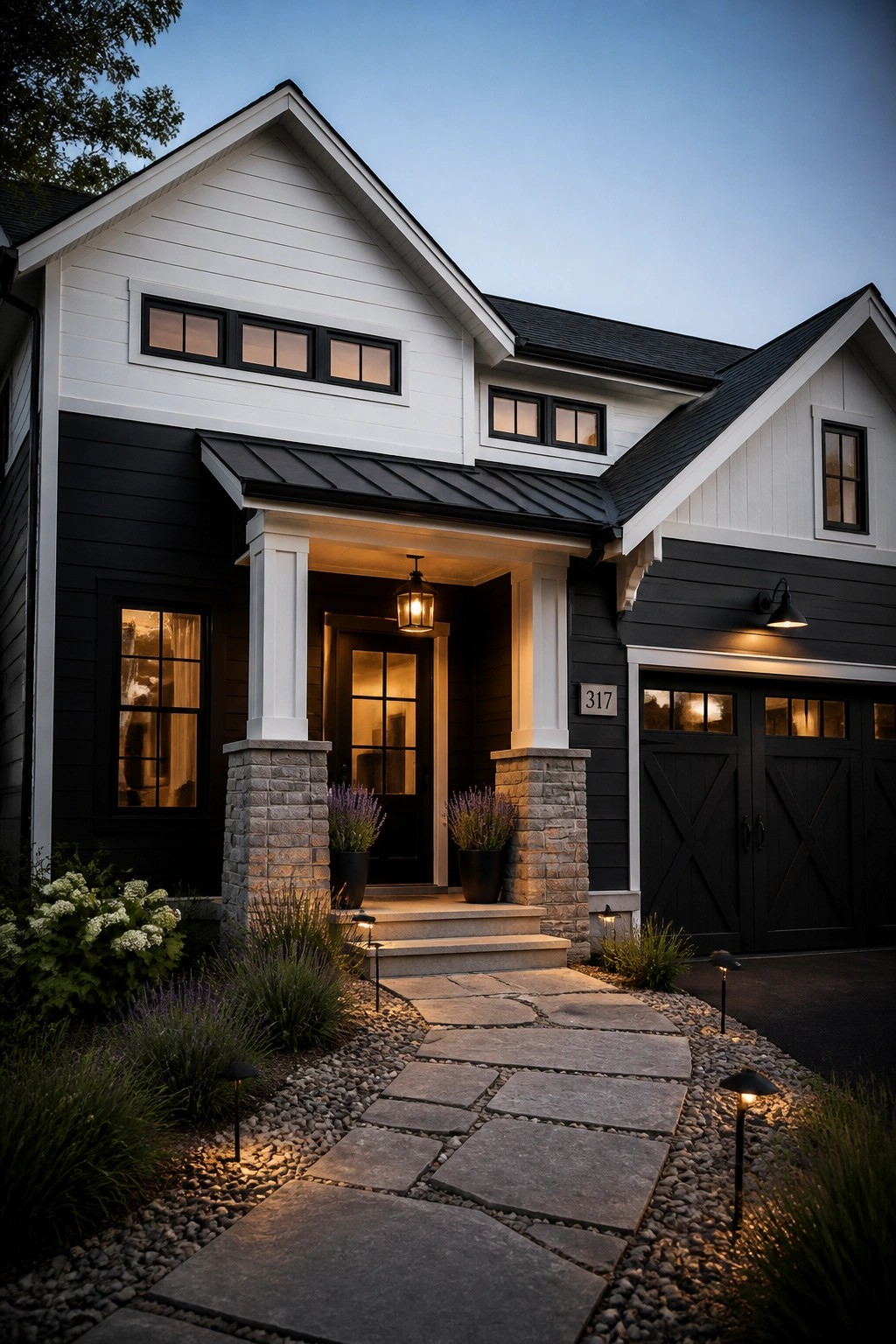 Modern black-and-white house with stone porch, lit pathway, and garage at dusk.
